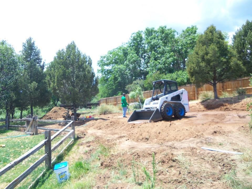 Small skid-steer loader working on a dirt slope near a fence and trees on a sunny day