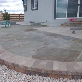 Curved concrete patio with stone border beside a house and gravel landscaping.