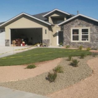 Suburban house with stone facade, open garage, and xeriscaped front yard under clear blue sky