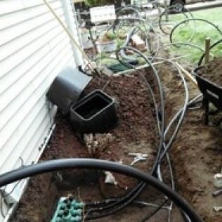 Yard beside house with hoses, black planters, and garden hoses strewn over bare dirt and mulch.