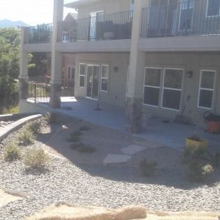 Modern house patio with gravel landscaping, stone columns, and upstairs balcony in bright sunlight