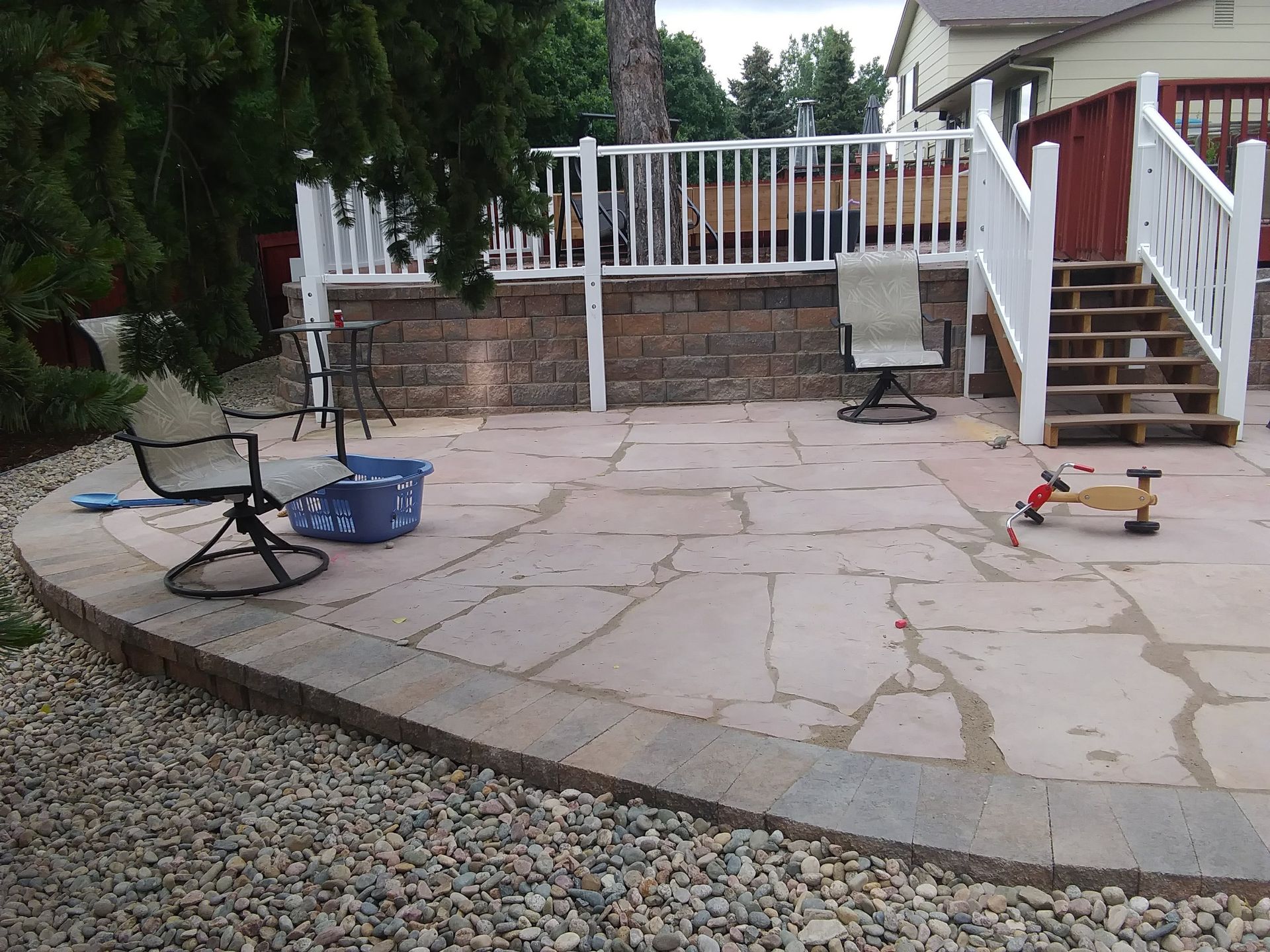 Backyard patio with chairs, a small table, a toy scooter, and white deck stairs with railing