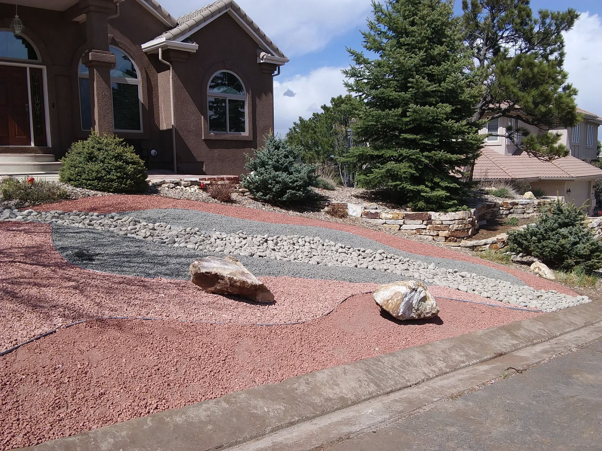 Landscaped front yard with red gravel, rocks, shrubs, and a brick house