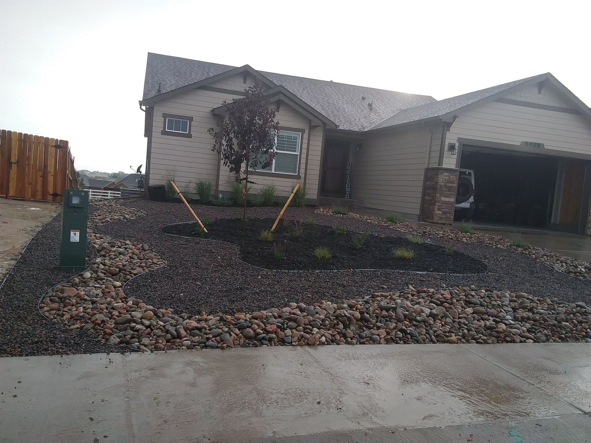 House with a garage, rock landscaping, and a green utility box on a wet driveway.
