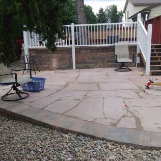 Backyard stone patio with white railing, chairs, blue basket, and a toy on the ground