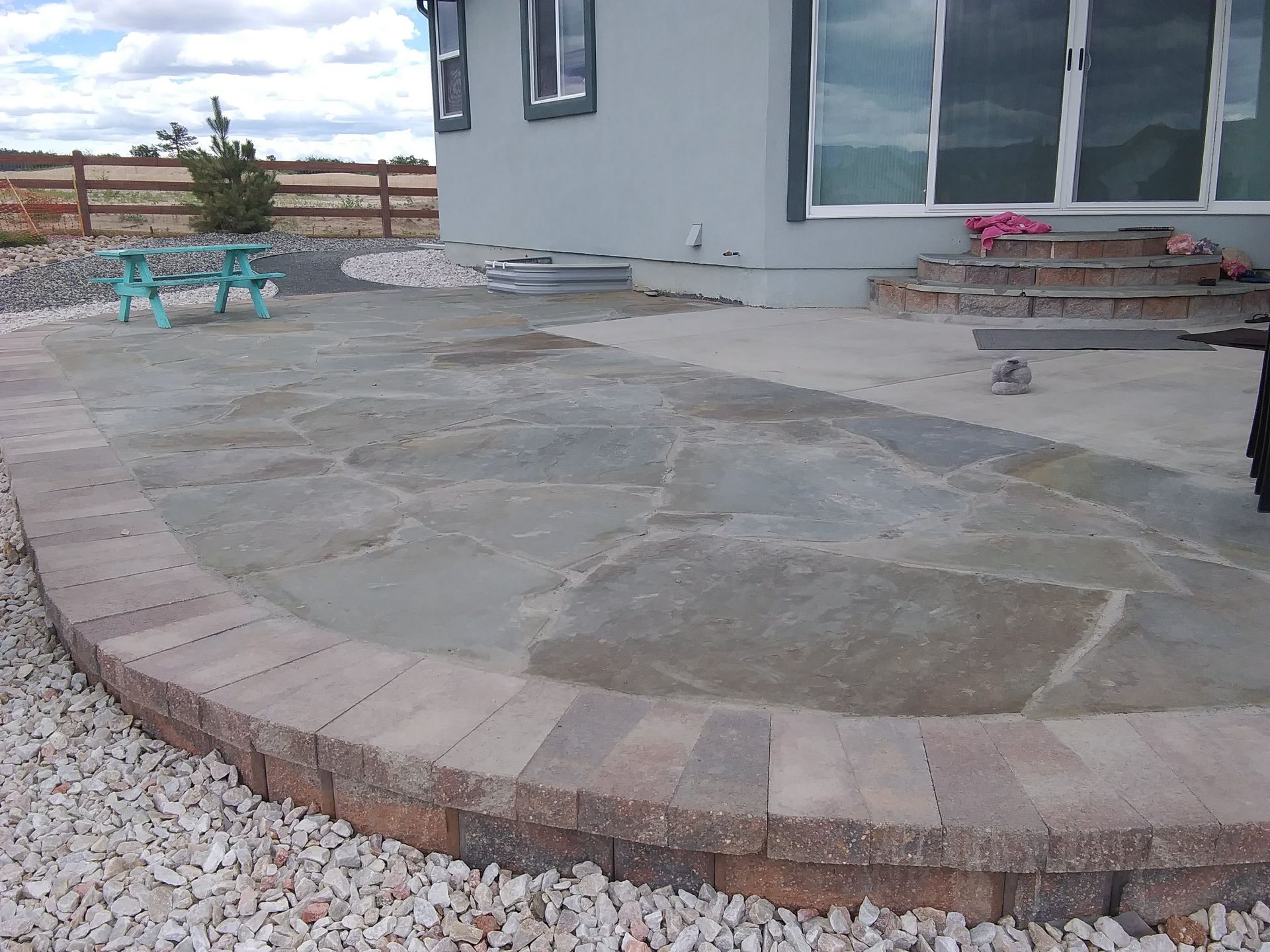 Patio with stamped concrete and brick border beside a house, with turquoise chairs and a small flower pot