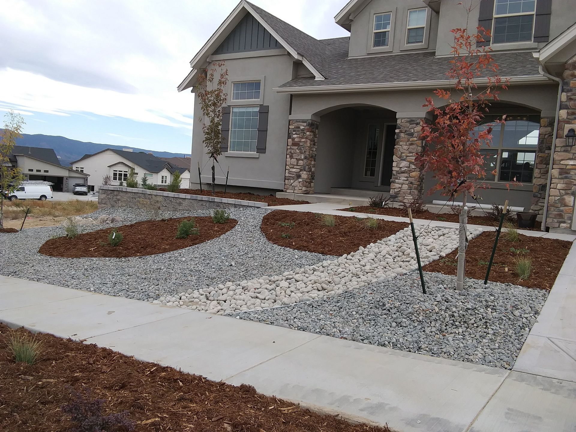 Newly built gray house with stone accents and landscaped front yard with gravel and young trees