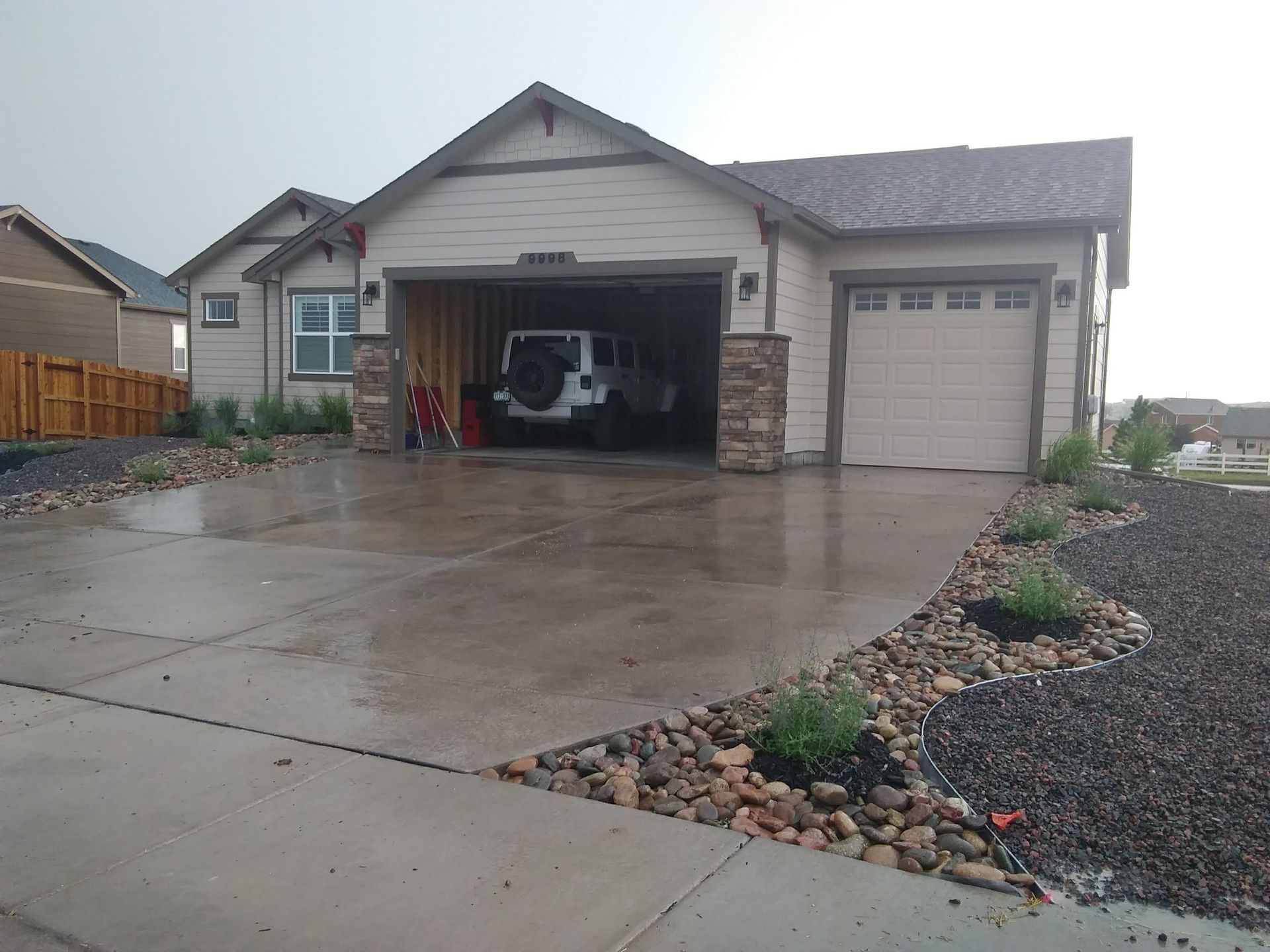 Wet suburban house with open garage and driveway, overcast day