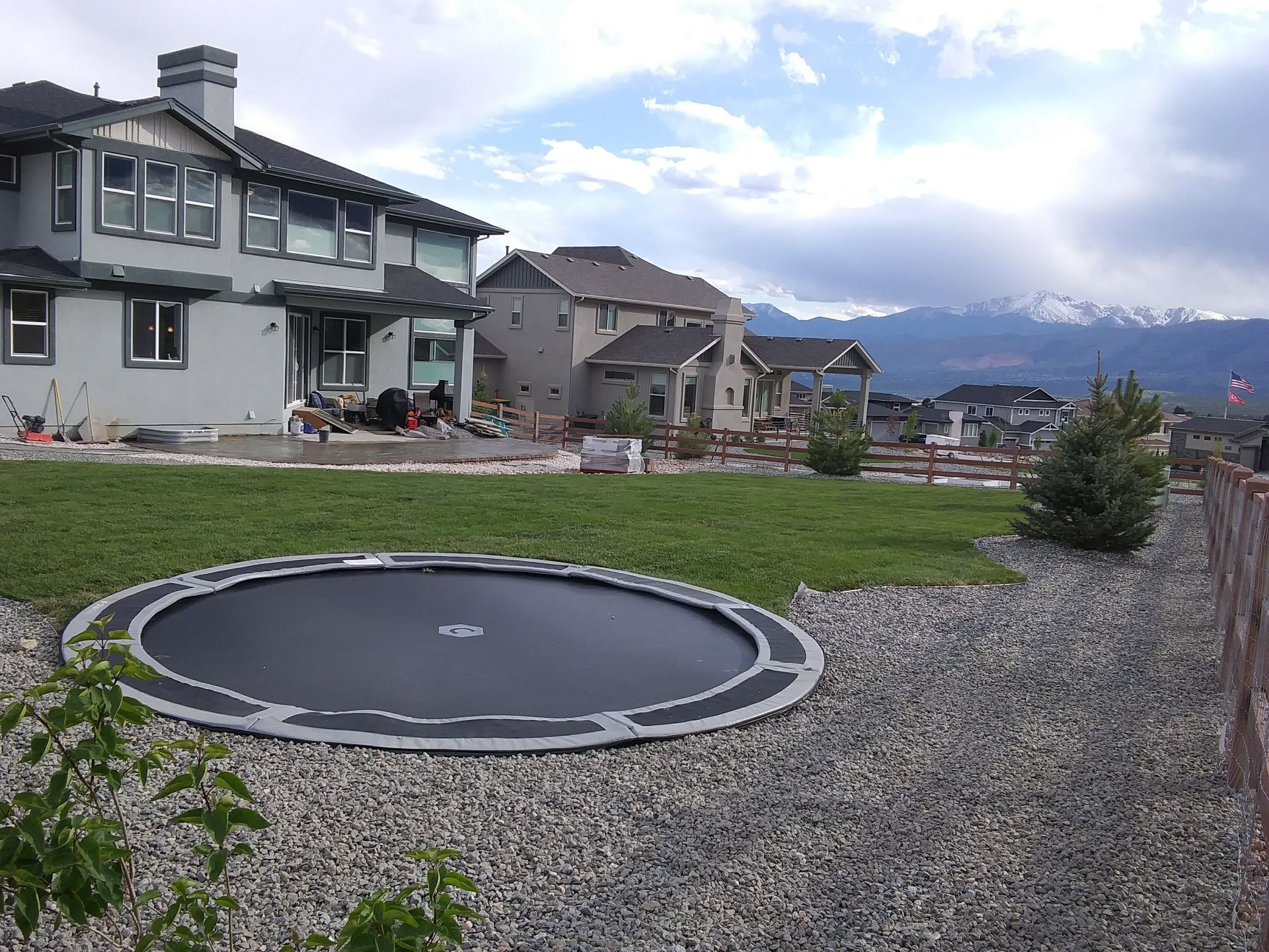 Backyard with a trampoline, suburban houses, and snow-capped mountains under a cloudy sky