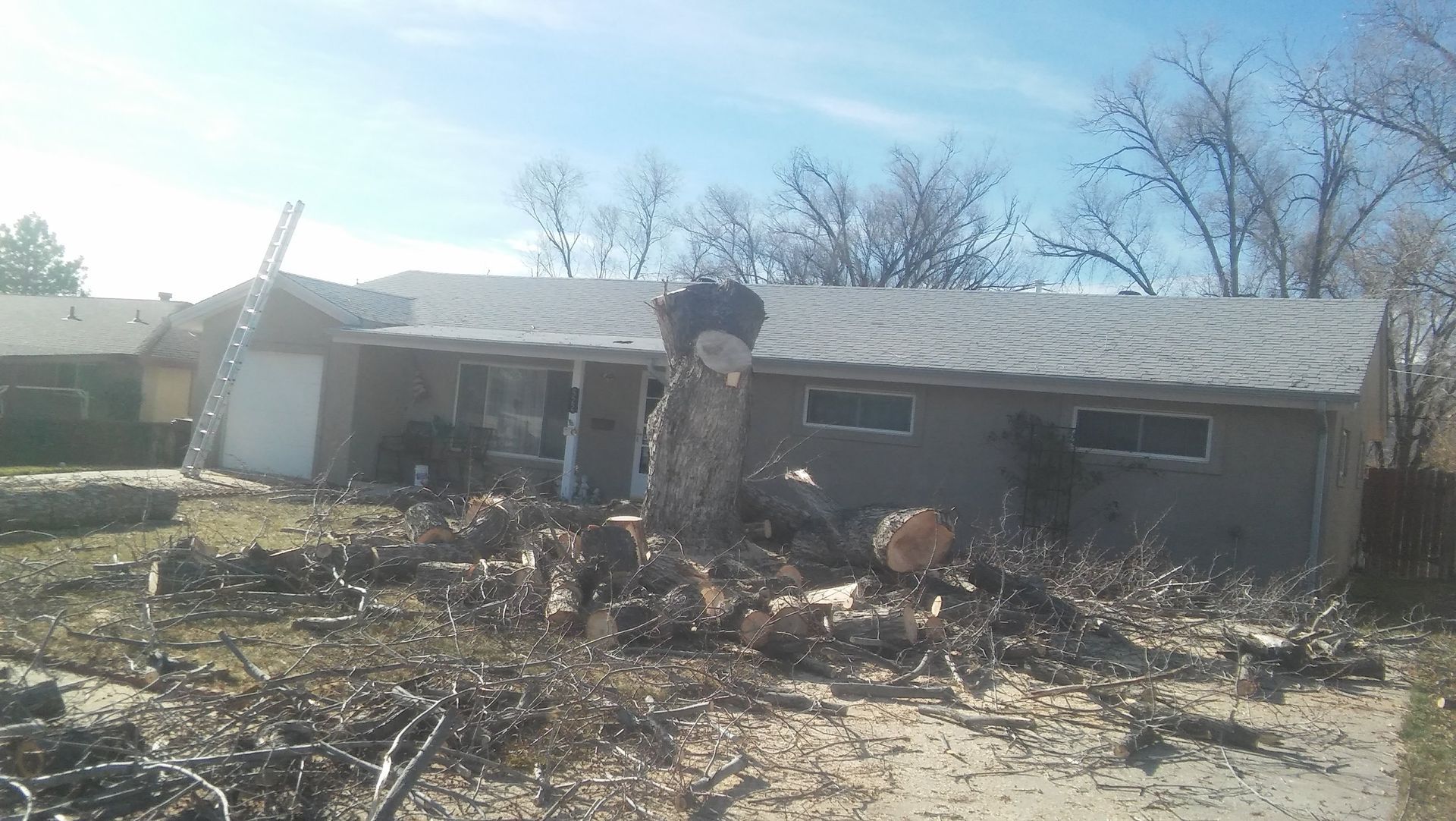 Small single-story house with a damaged roof and sparse front yard under bright sunlight