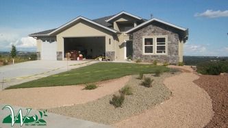 Modern single-story house with open garage, landscaped yard, and curved gravel driveway under a clear sky