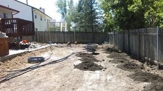 Backyard under construction with dirt, hoses, and a wooden fence on a sunny day