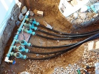 Blue utility valves and black pipes in a dirt trench at a construction site.