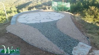 Gravel and concrete mosaic path with a circular stone design in a landscaped outdoor area