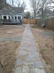 Stone walkway leading through a backyard to a wooden fence, with a house and deck on the left.