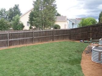 Backyard with green lawn, wooden fence, trees, and two large metal tanks by the right side.