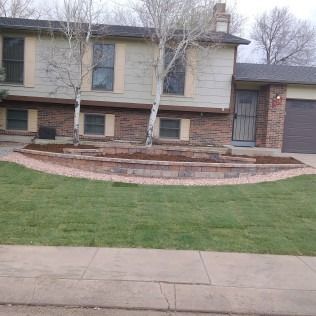 Suburban house with a curved brick retaining wall and green lawn beside a sidewalk