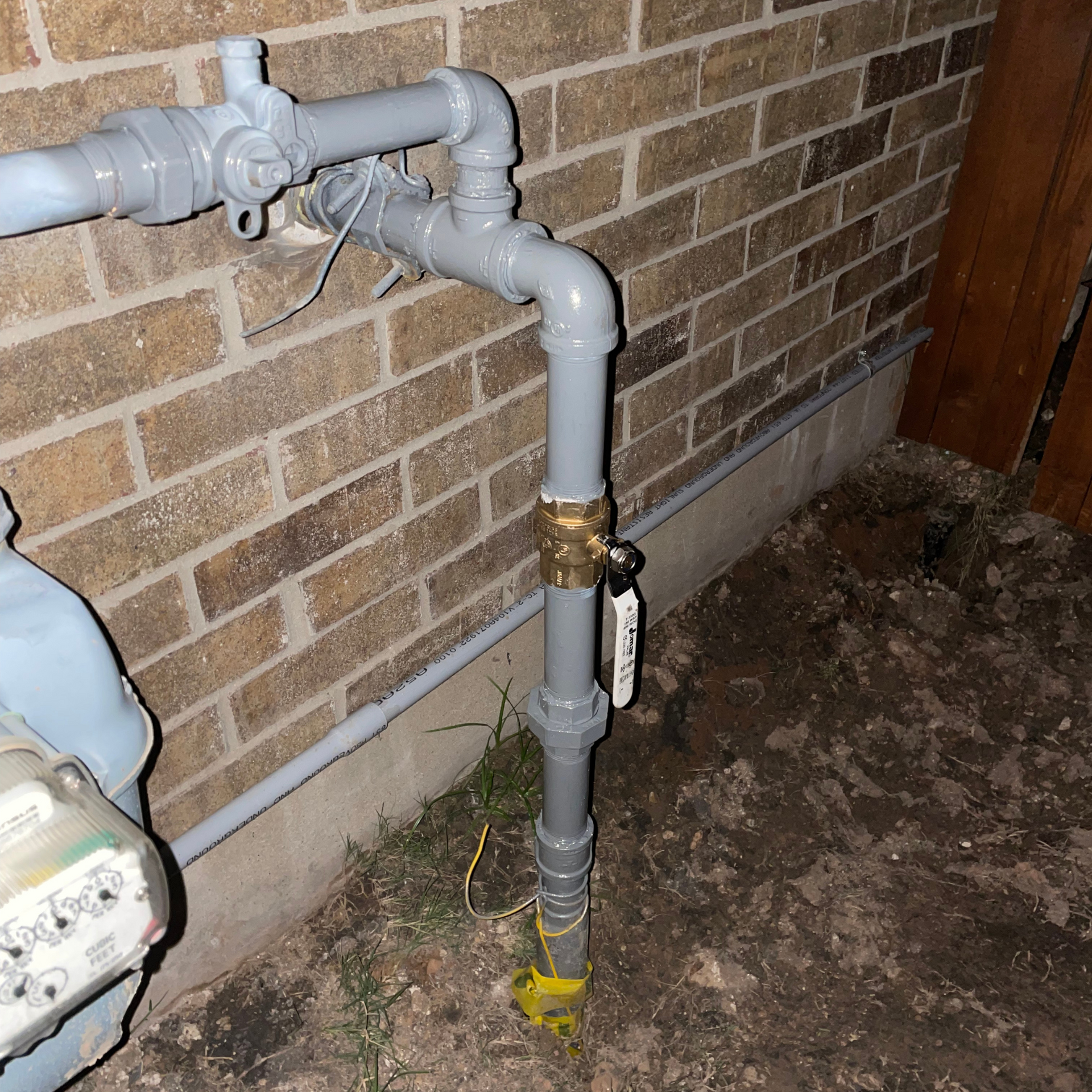 Gray gas pipes against a brick wall, with a valve and meter visible.