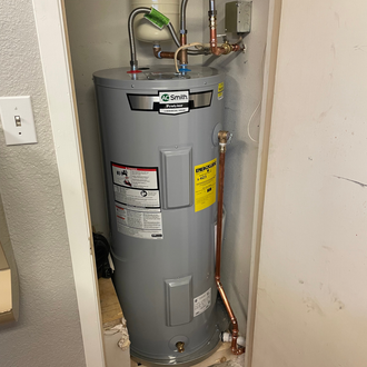 A water heater unit installed in a closet. Gray cylinder with copper pipes and various warning labels.