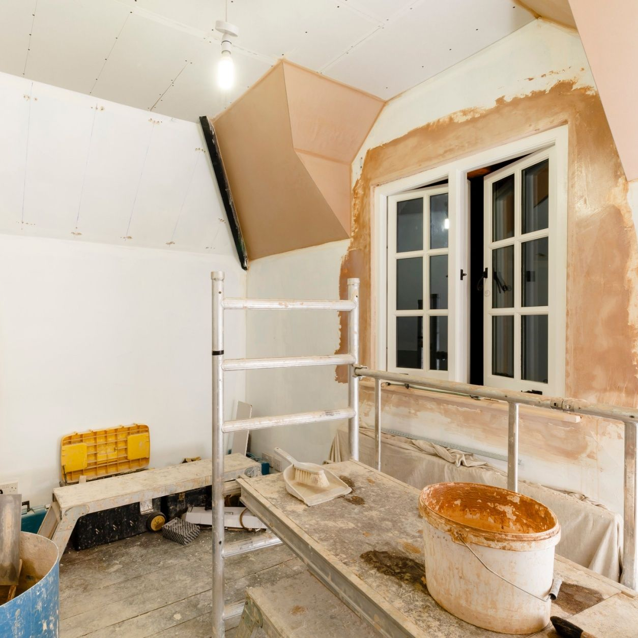 Room under renovation with open window, scaffolding, and tools.
