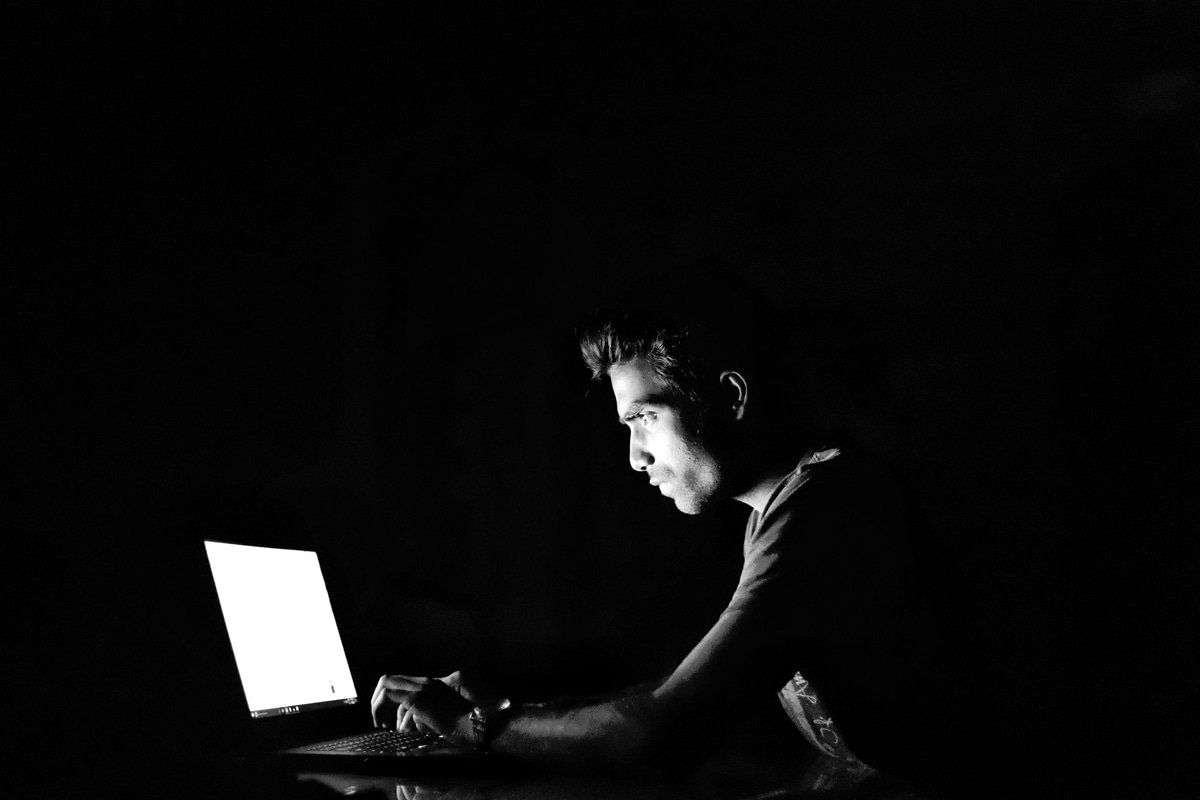 A man with a computer in a dark room looking for a criminal attorney to fight his fraud charges.