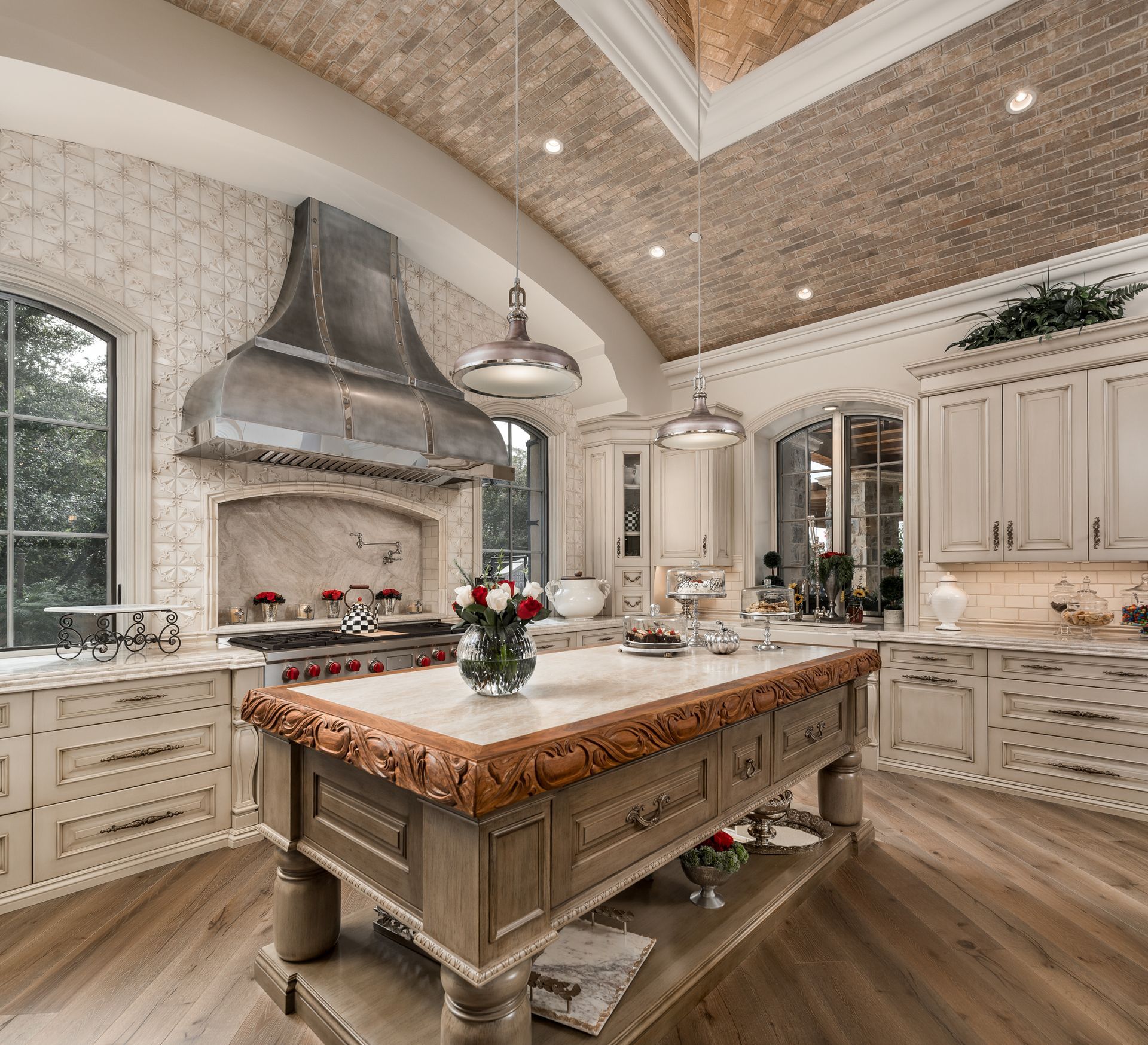 French kitchen with large island, marble countertops, white cabinetry, arched brick ceiling, and a stainless range hood
