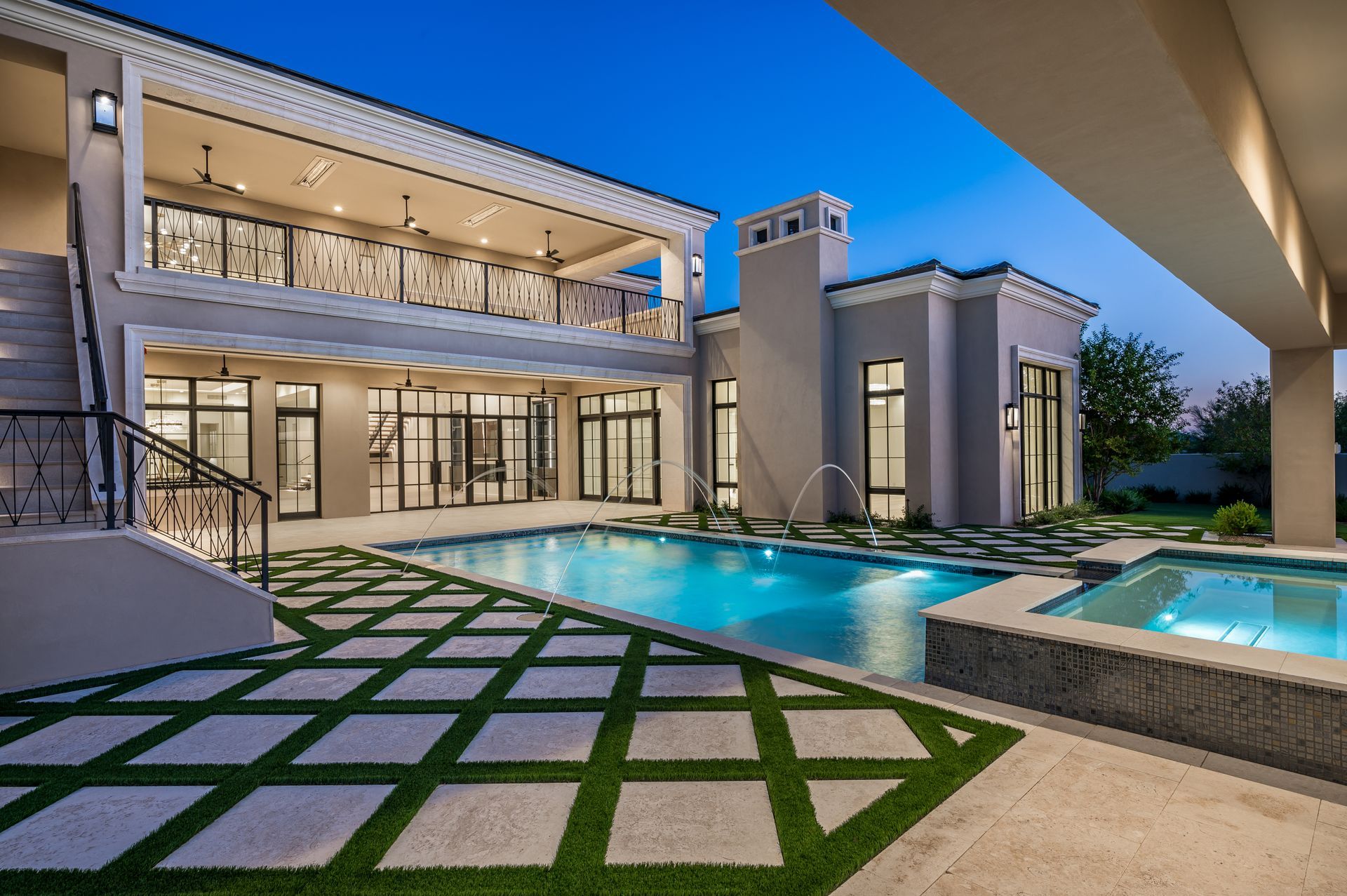 Modern luxury home with illuminated pool, glass walls, and geometric stone patio at dusk