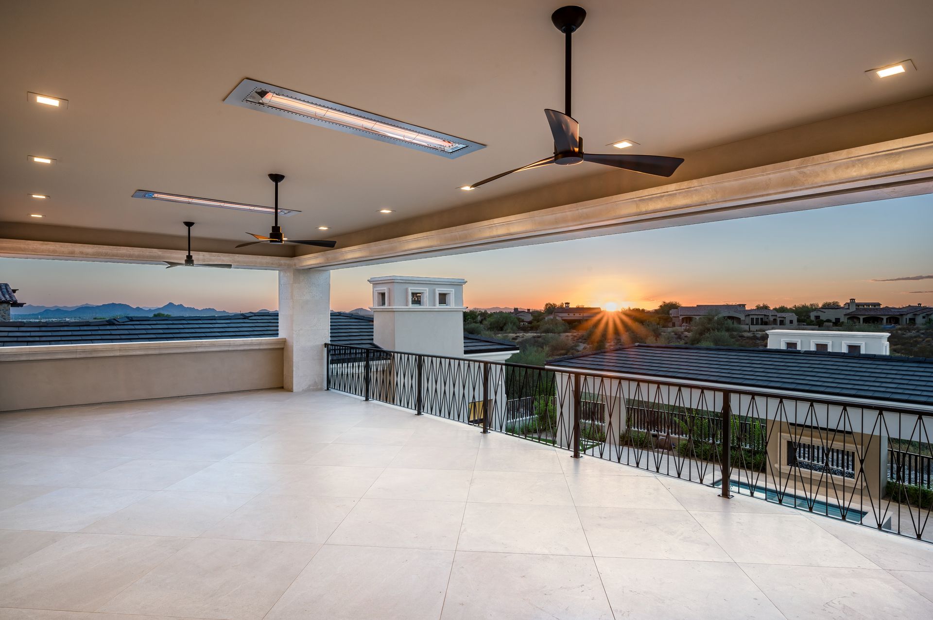 Rooftop terrace at sunset with white flooring, black railing, and ceiling fans overlooking a city skyline