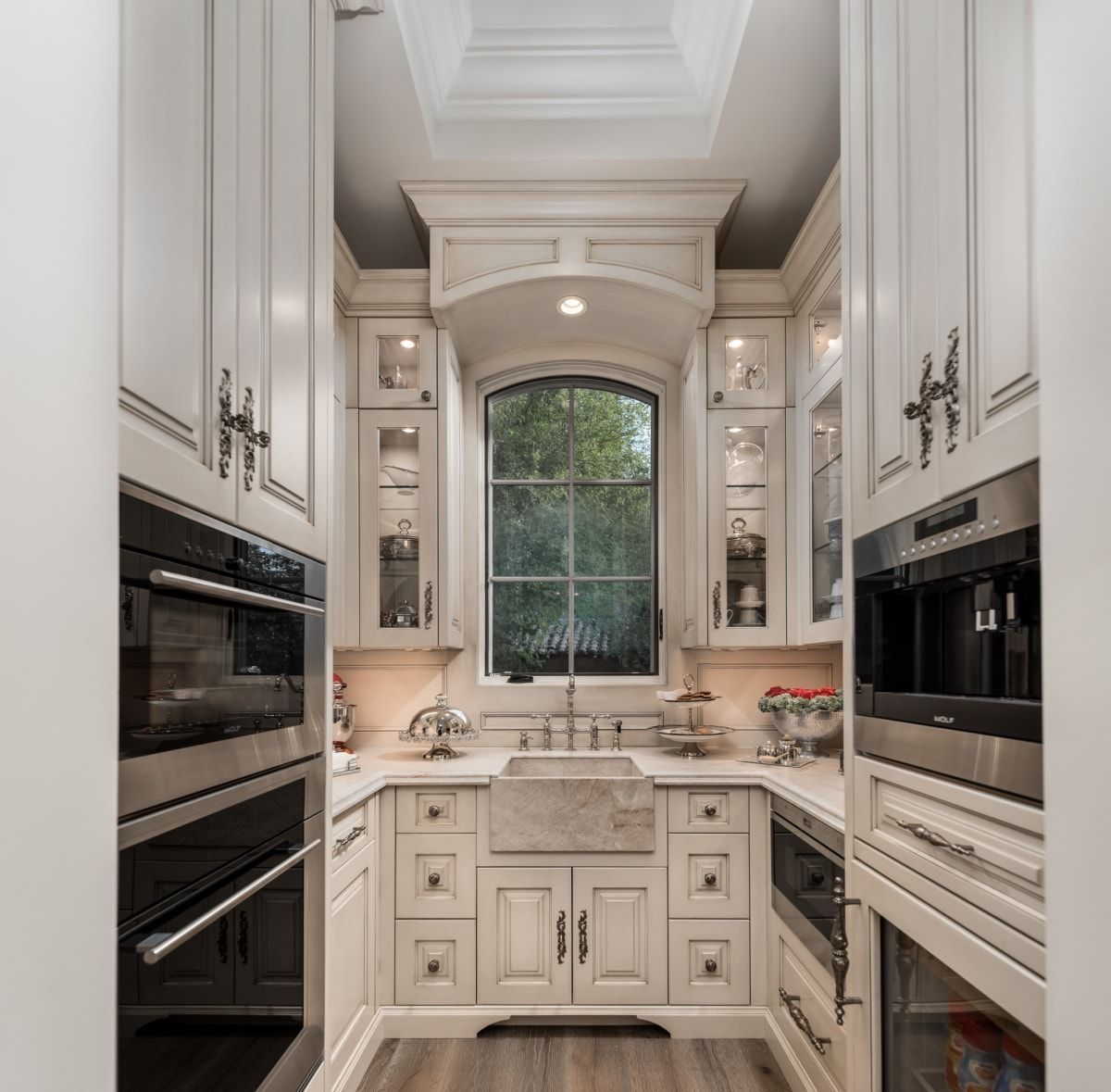 French white gourmet butlers kitchen with built-in ovens, marble countertops, and a window