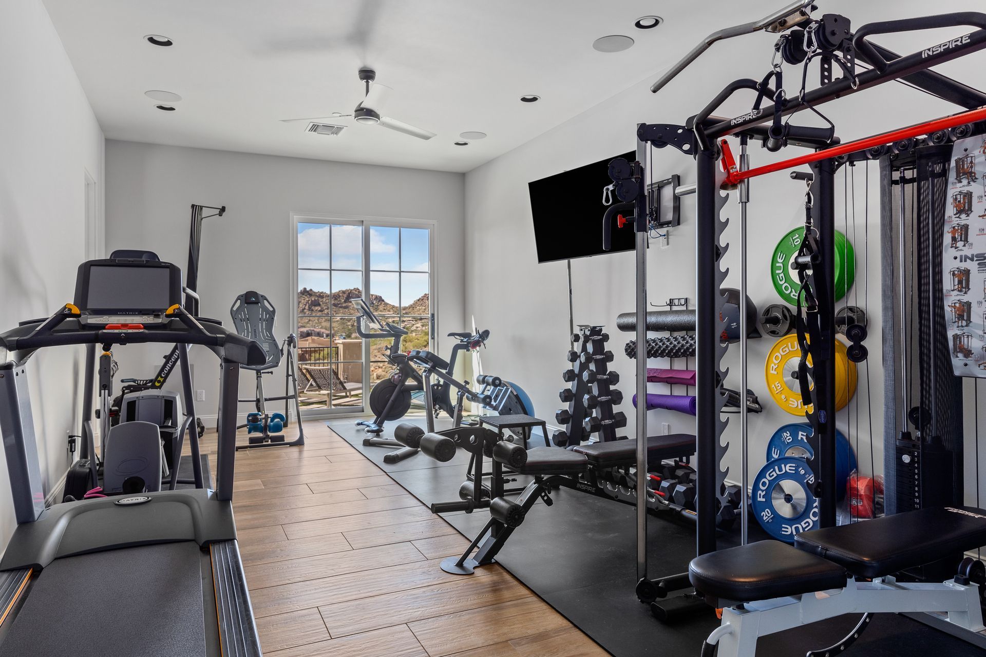 Home gym with treadmill, weight rack, and bench by a large window showing construction outside