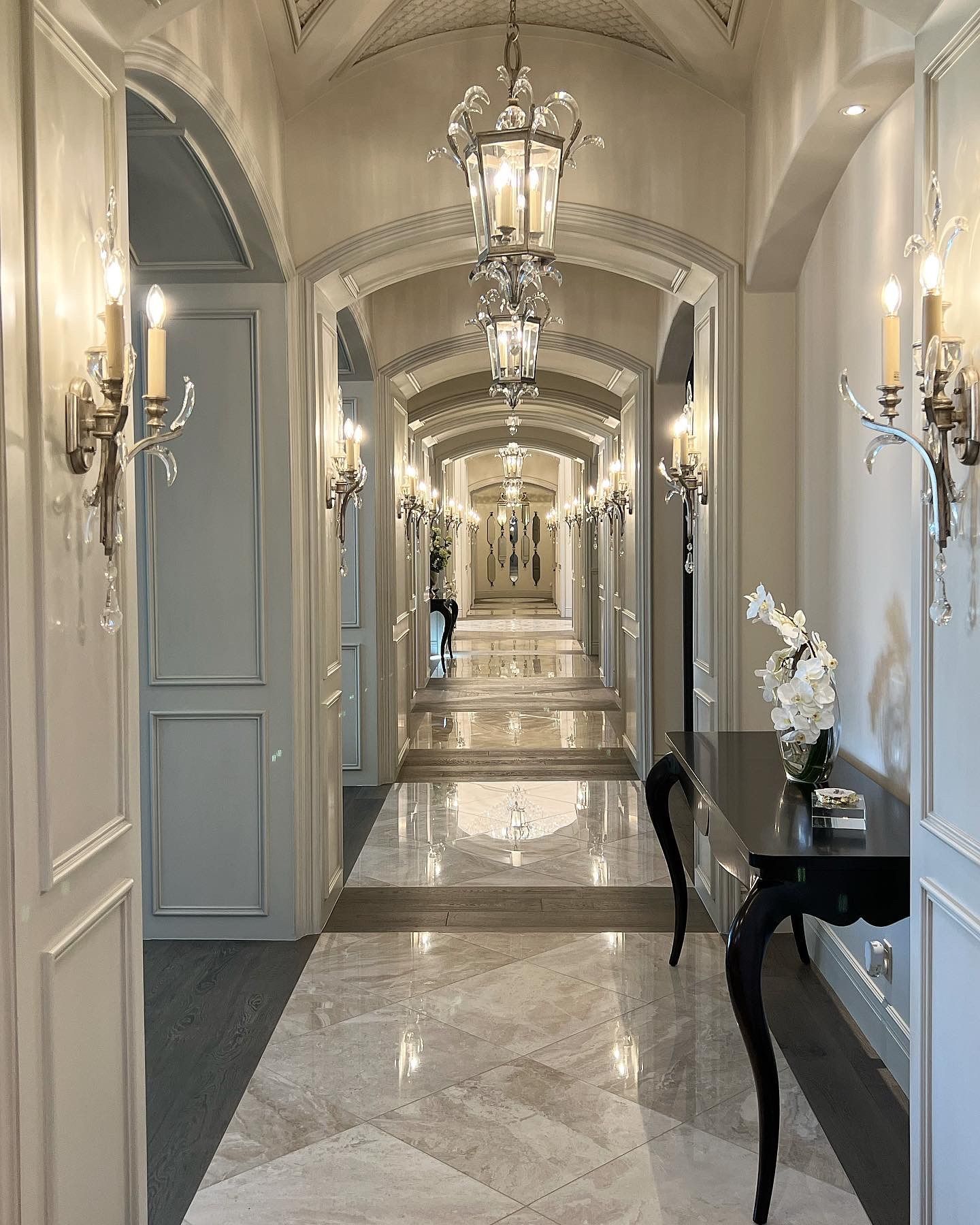 luxury home hallway with wood and marble flooring, ornate light fixtures and arches