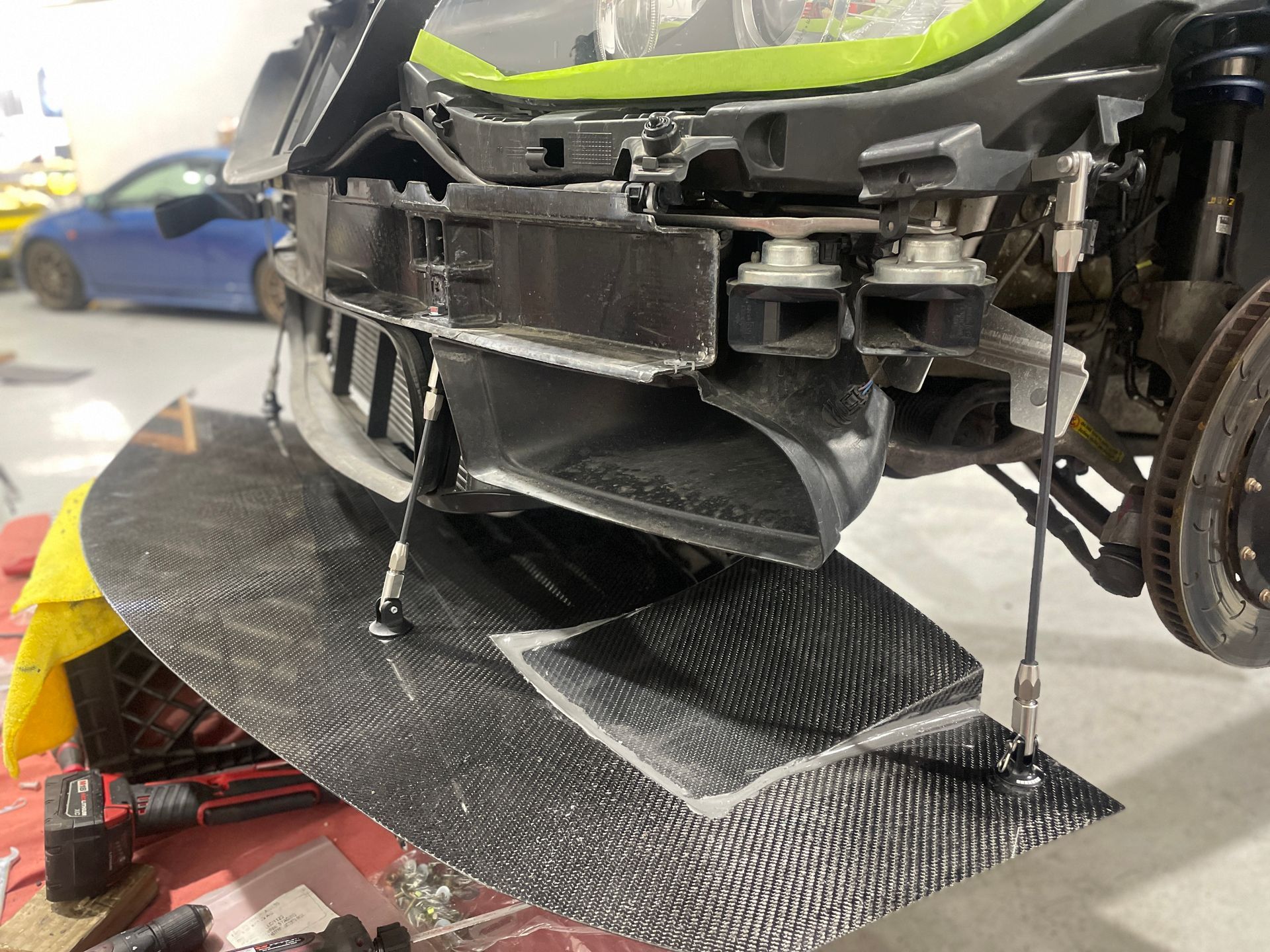 Car with front bumper removed on a lift, exposing the dark undertray and front suspension.
