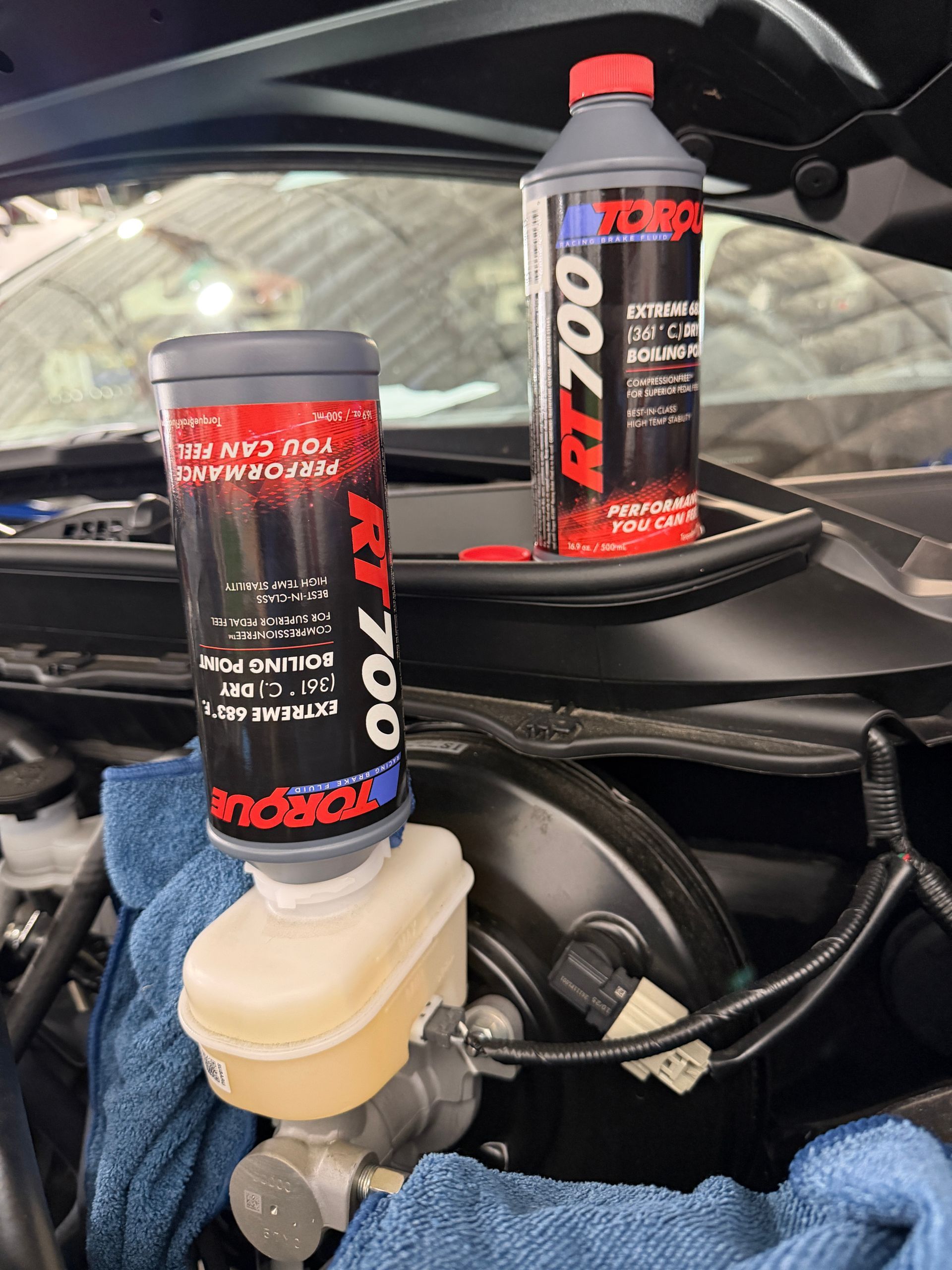 Two red-and-black Redline RT-700 bottles mounted on a car engine bay component.