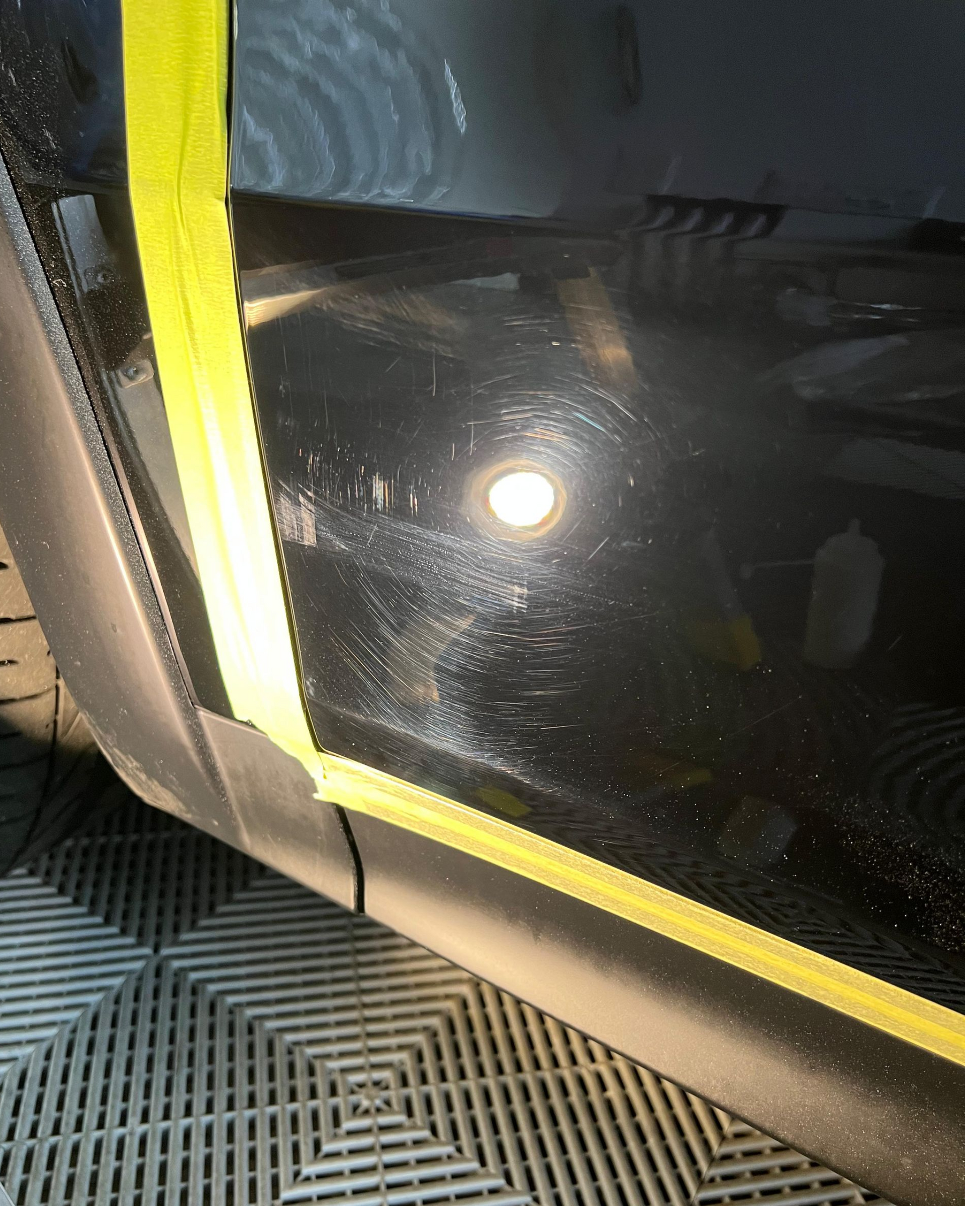 Person holding a phone reflected in a glossy black car pillar beside a beige vehicle interior