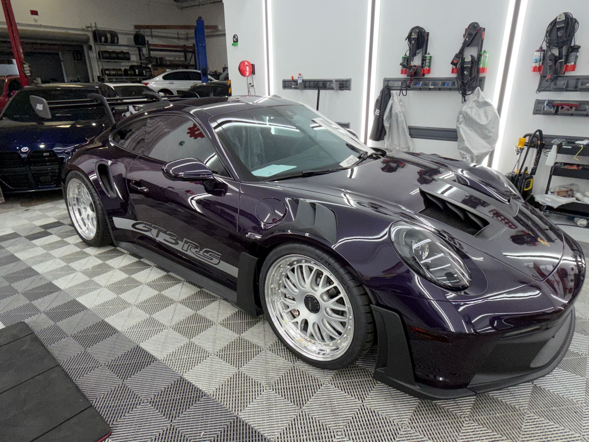 Car with front bumper removed on a lift, exposing the dark undertray and front suspension.
