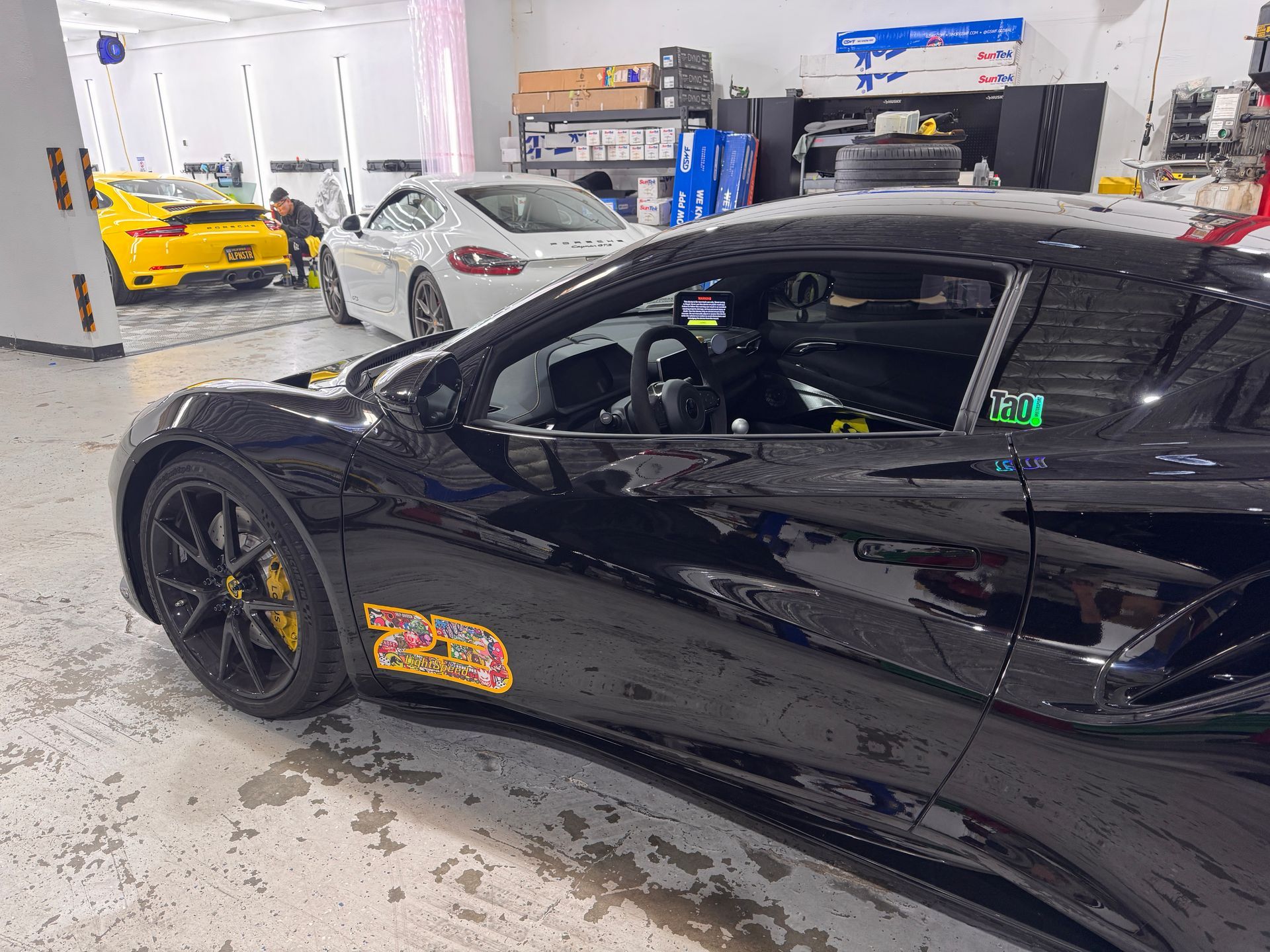 Black sports car with yellow brake calipers in a garage, with another sports car in the background