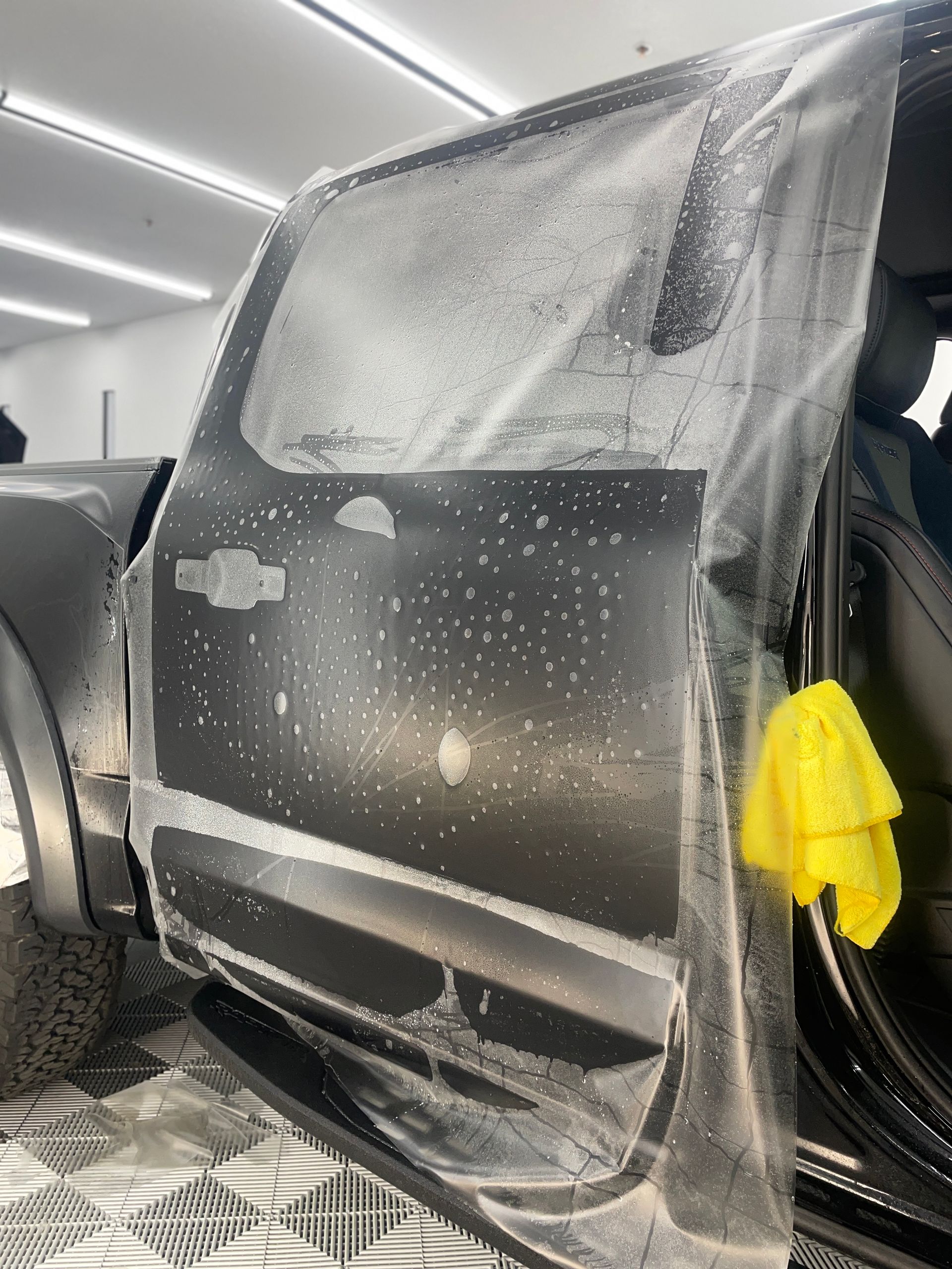 Black pickup truck side door covered in soap suds inside a car wash bay