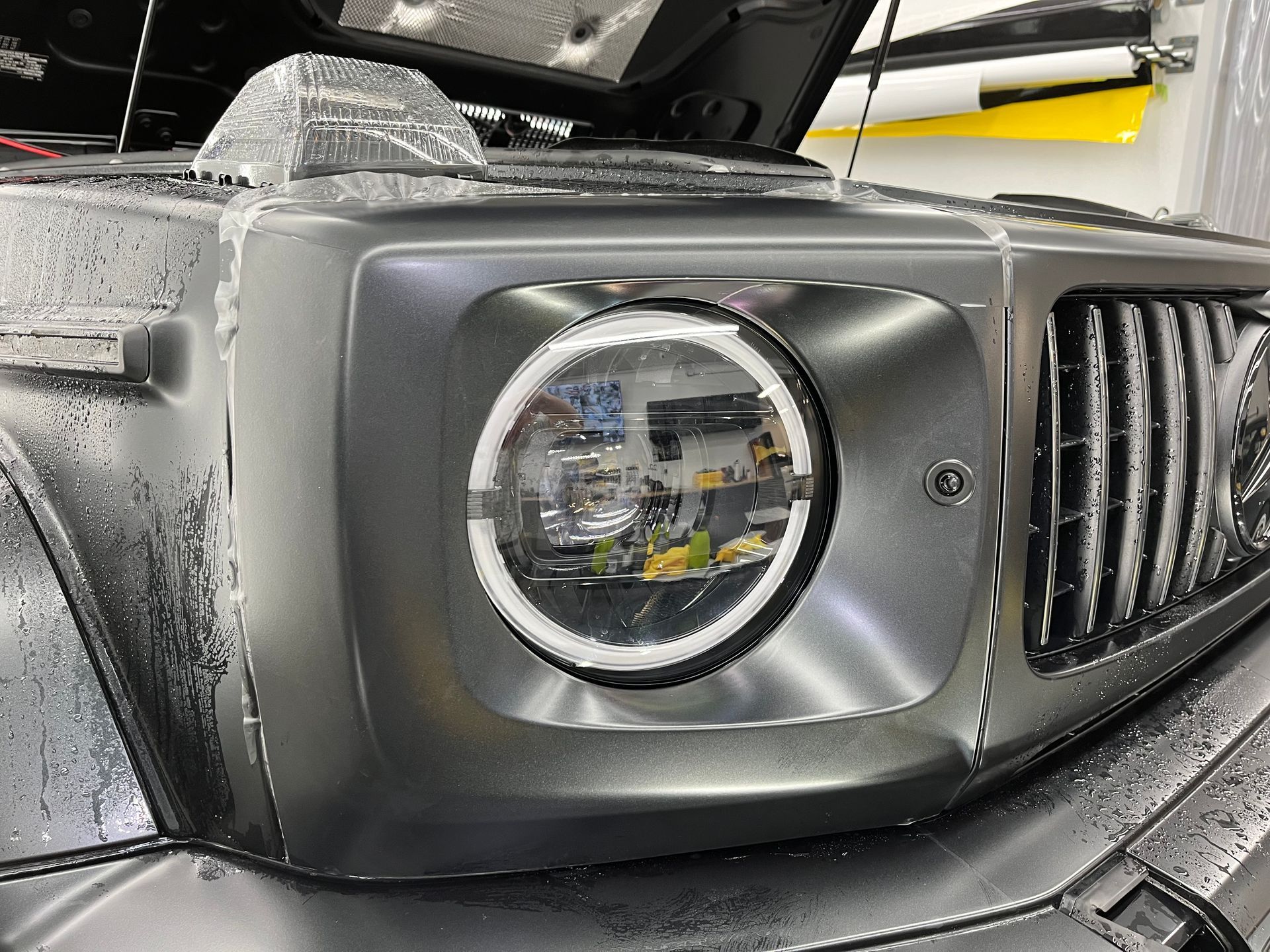 Close-up of a gray off-road vehicle’s round headlight and grille, splashed with mud.