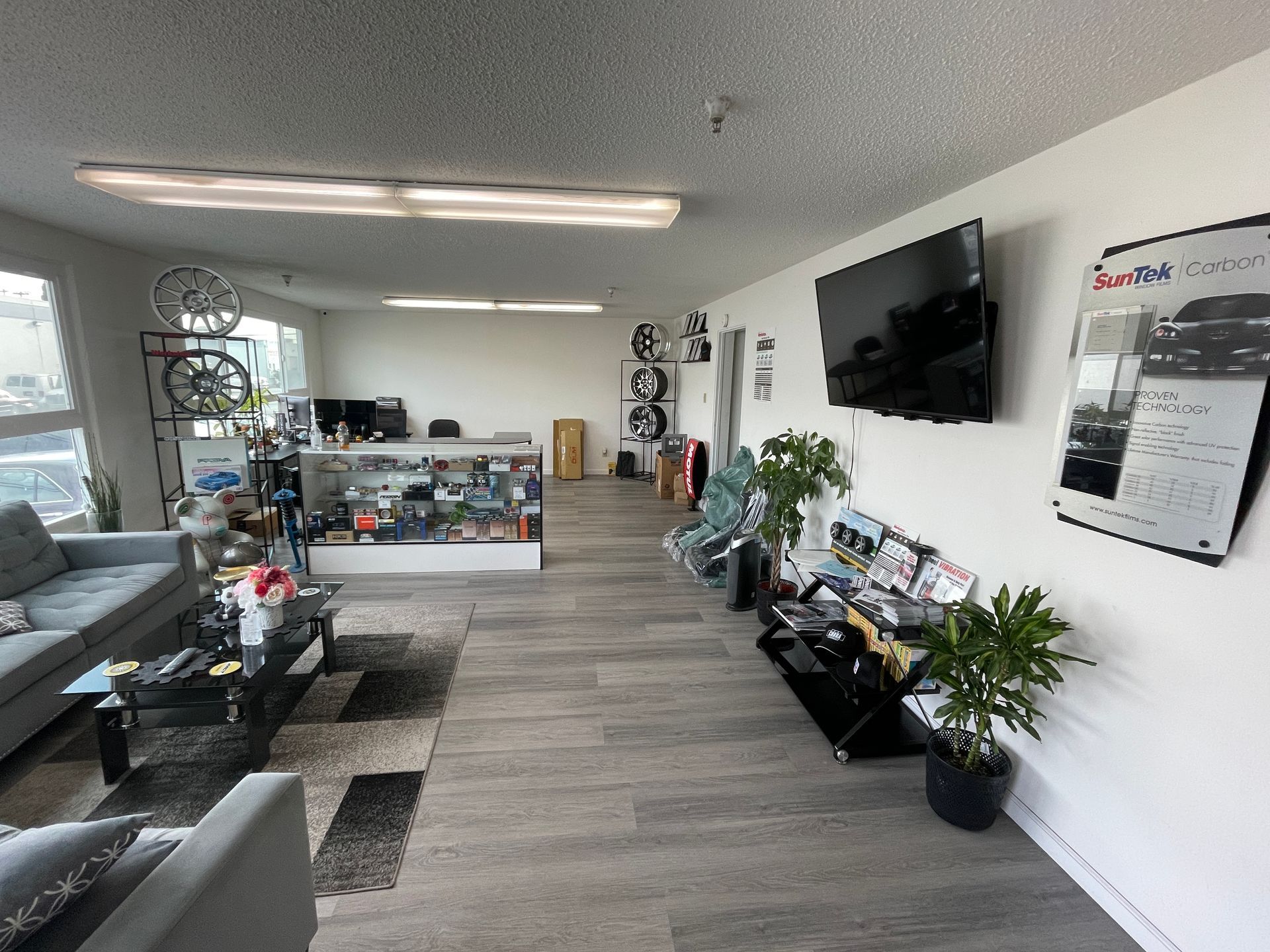 Bright modern office interior with couches, desks, plants, wall-mounted TV, and a reception area.