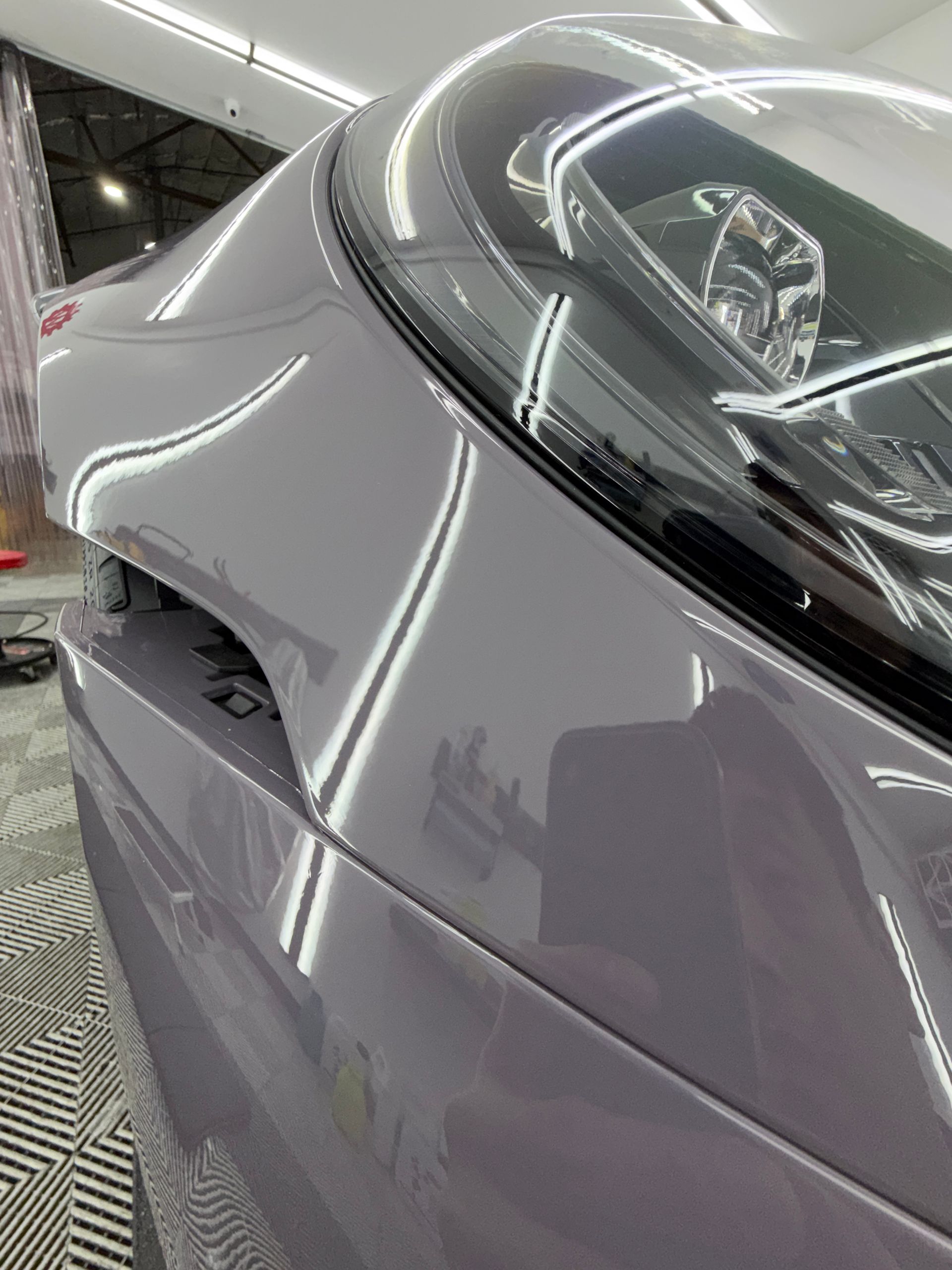 Close-up of a silver car’s rear quarter panel and taillight in a garage or showroom