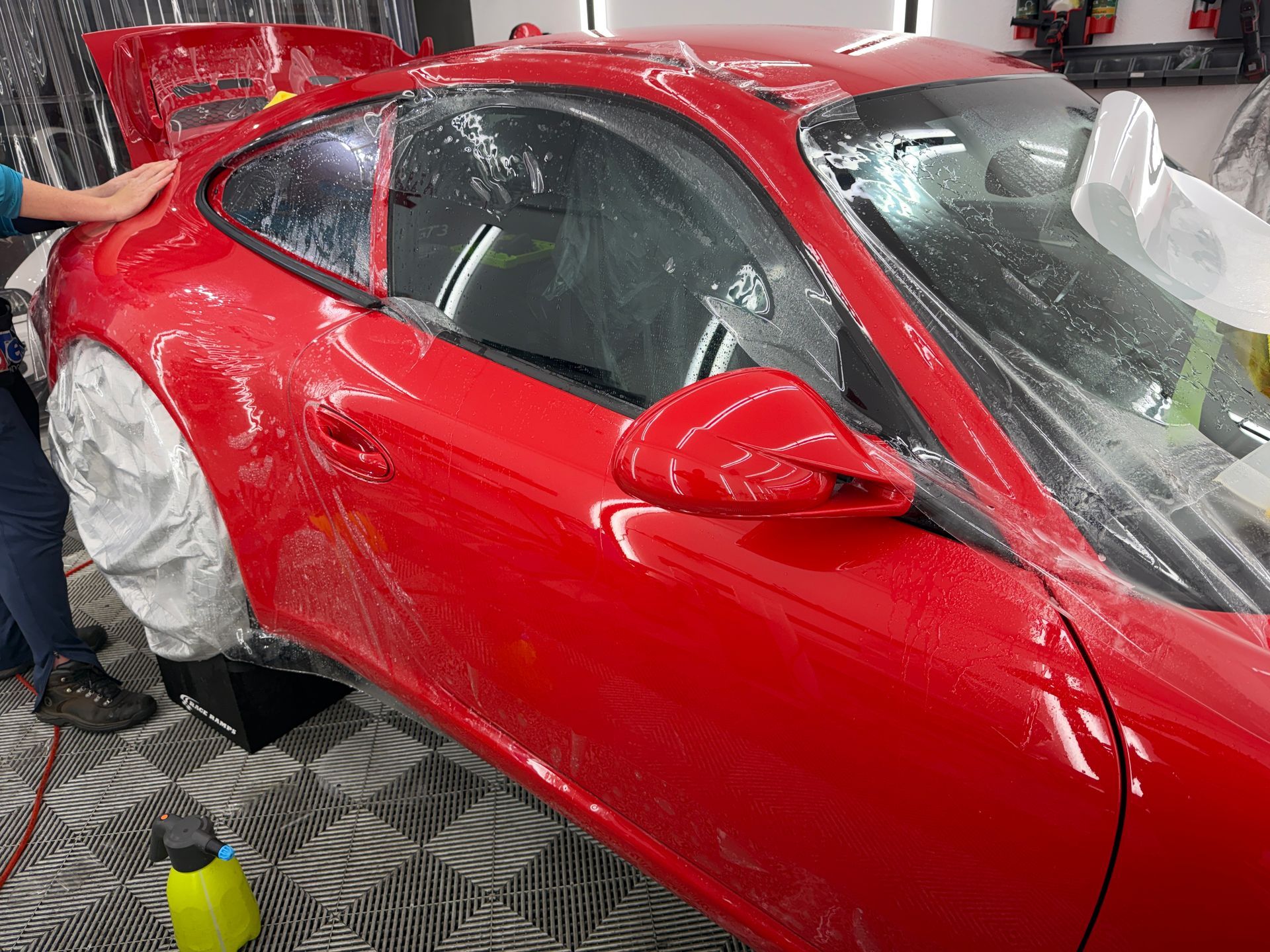 Red sports car being wrapped in protective plastic in a workshop