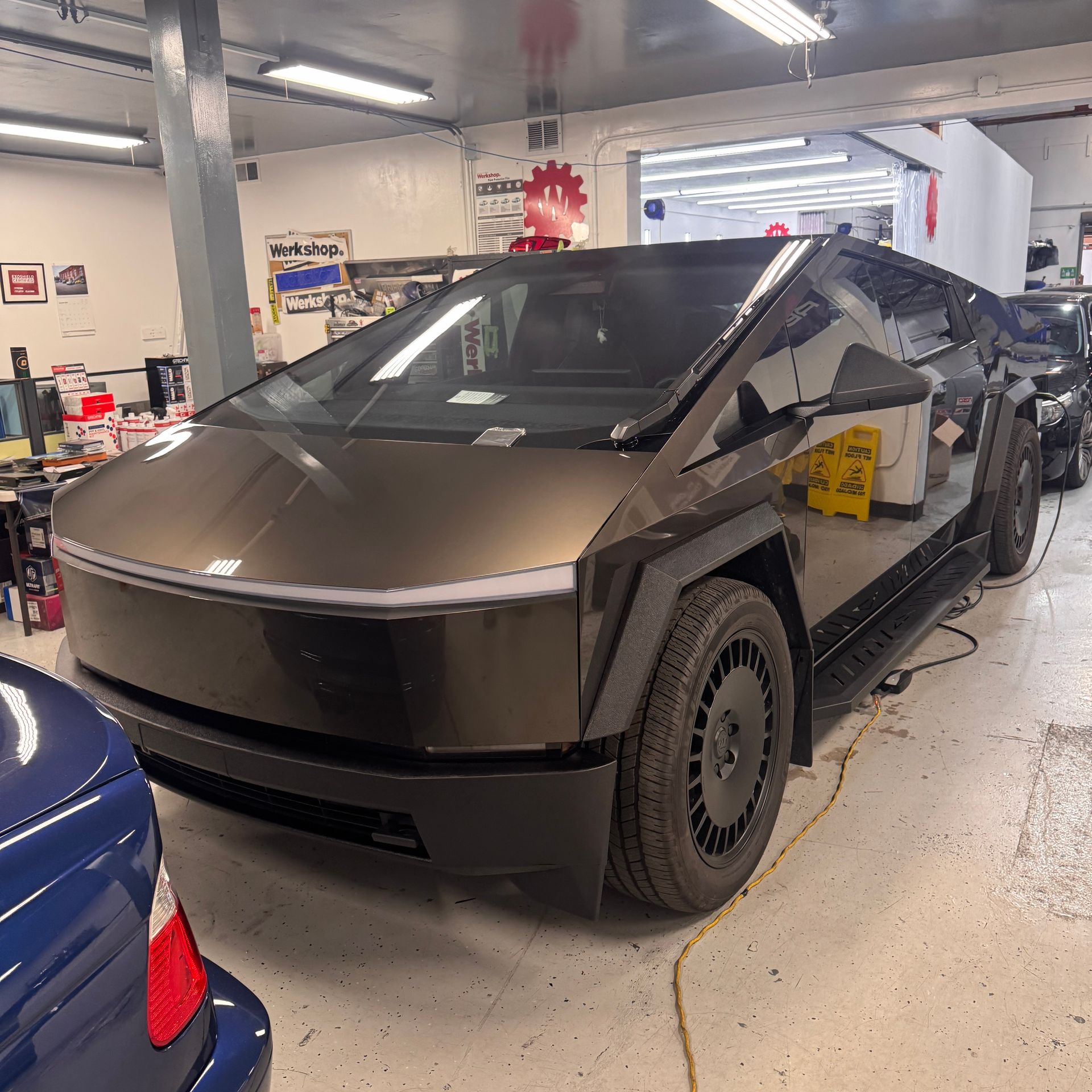 Cybertruck in an auto shop garage with a dark wrap and visible wheel covers