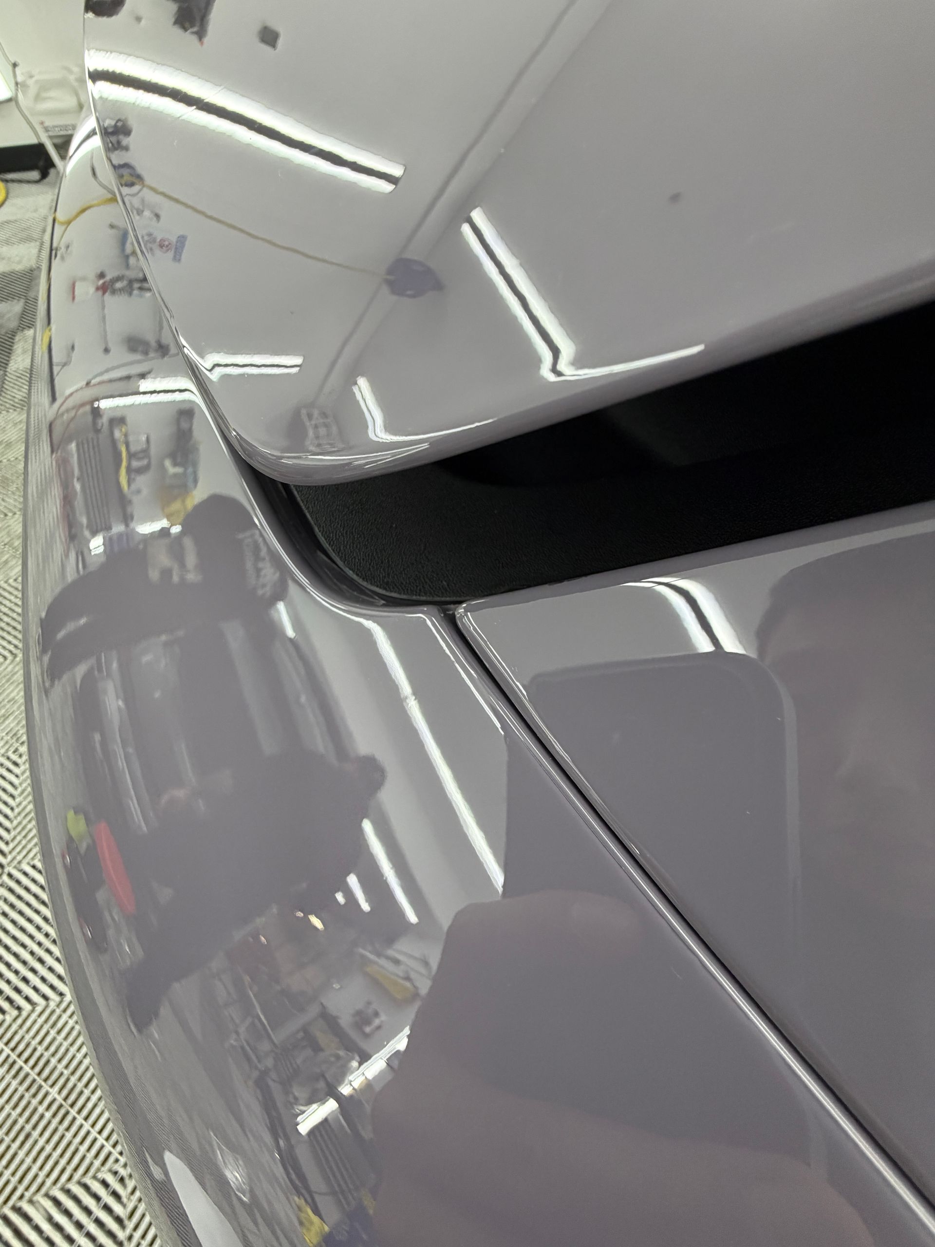 Close-up of a gray car panel with a visible seam and reflections from overhead lights in a garage.