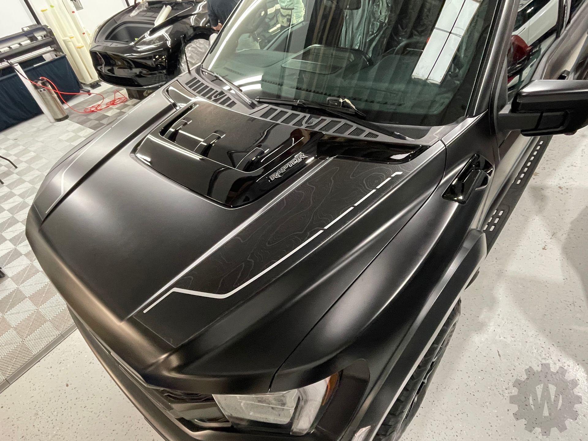 Black SUV hood with matte finish and hood scoop in a garage, viewed from above