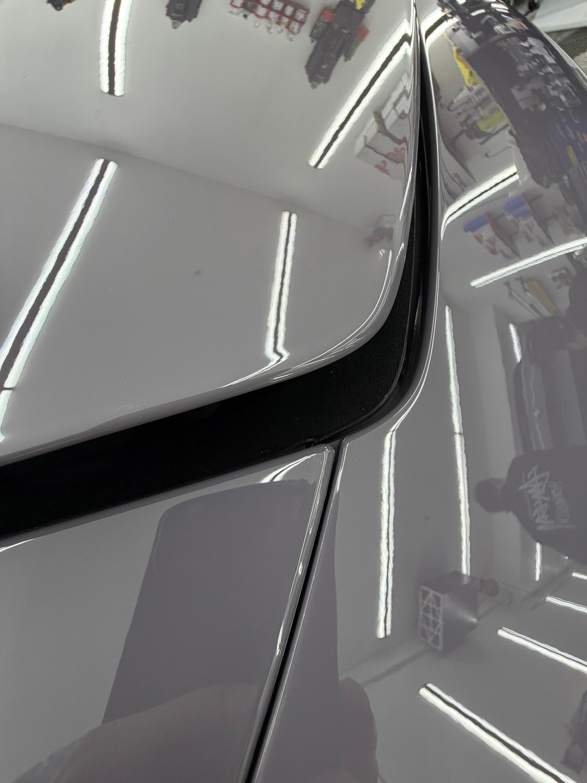 Close-up of a gray car’s hood and windshield seam under bright indoor lights