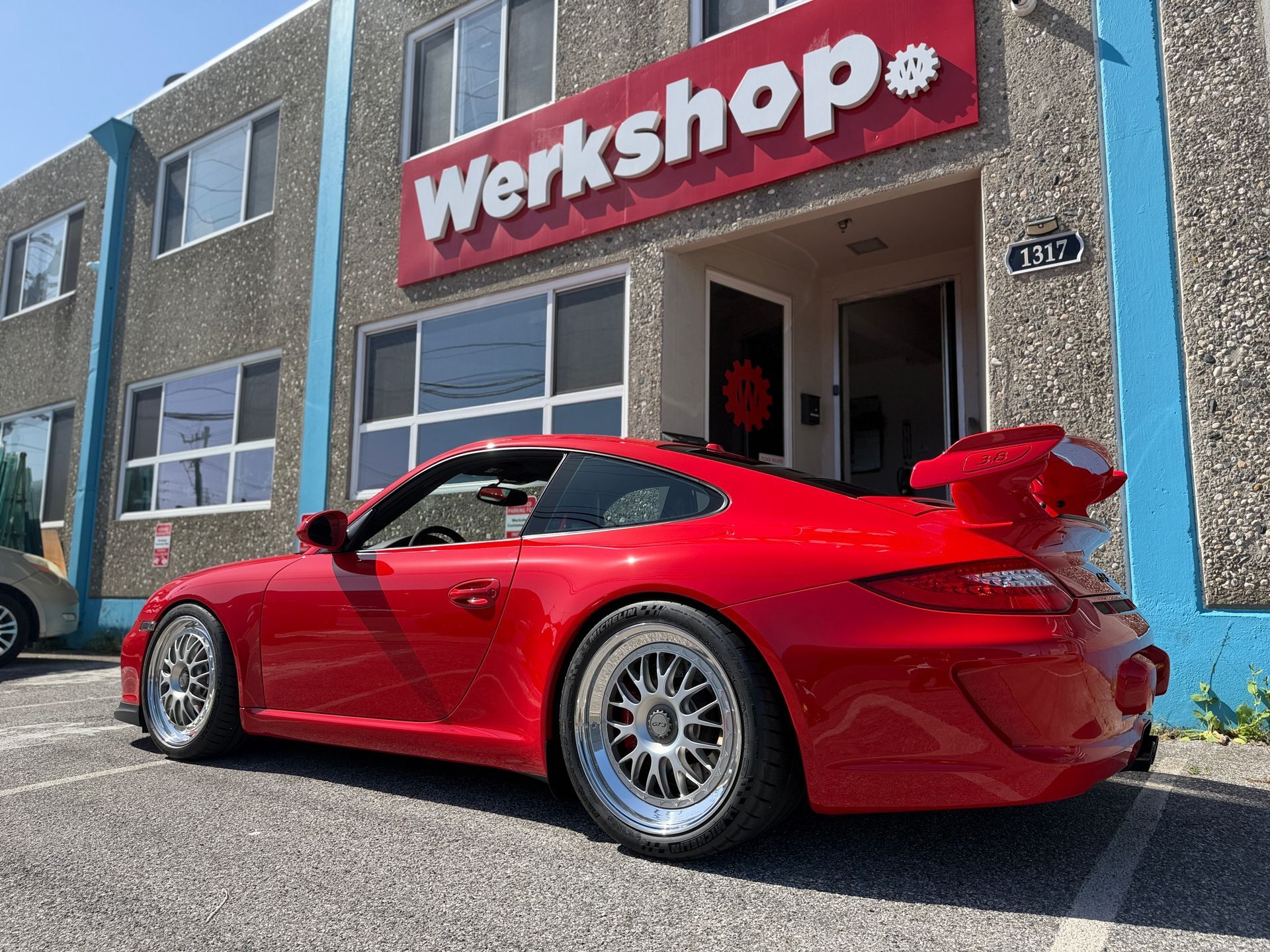 Red sports car parked outside a workshop garage with a red sign above the entrance