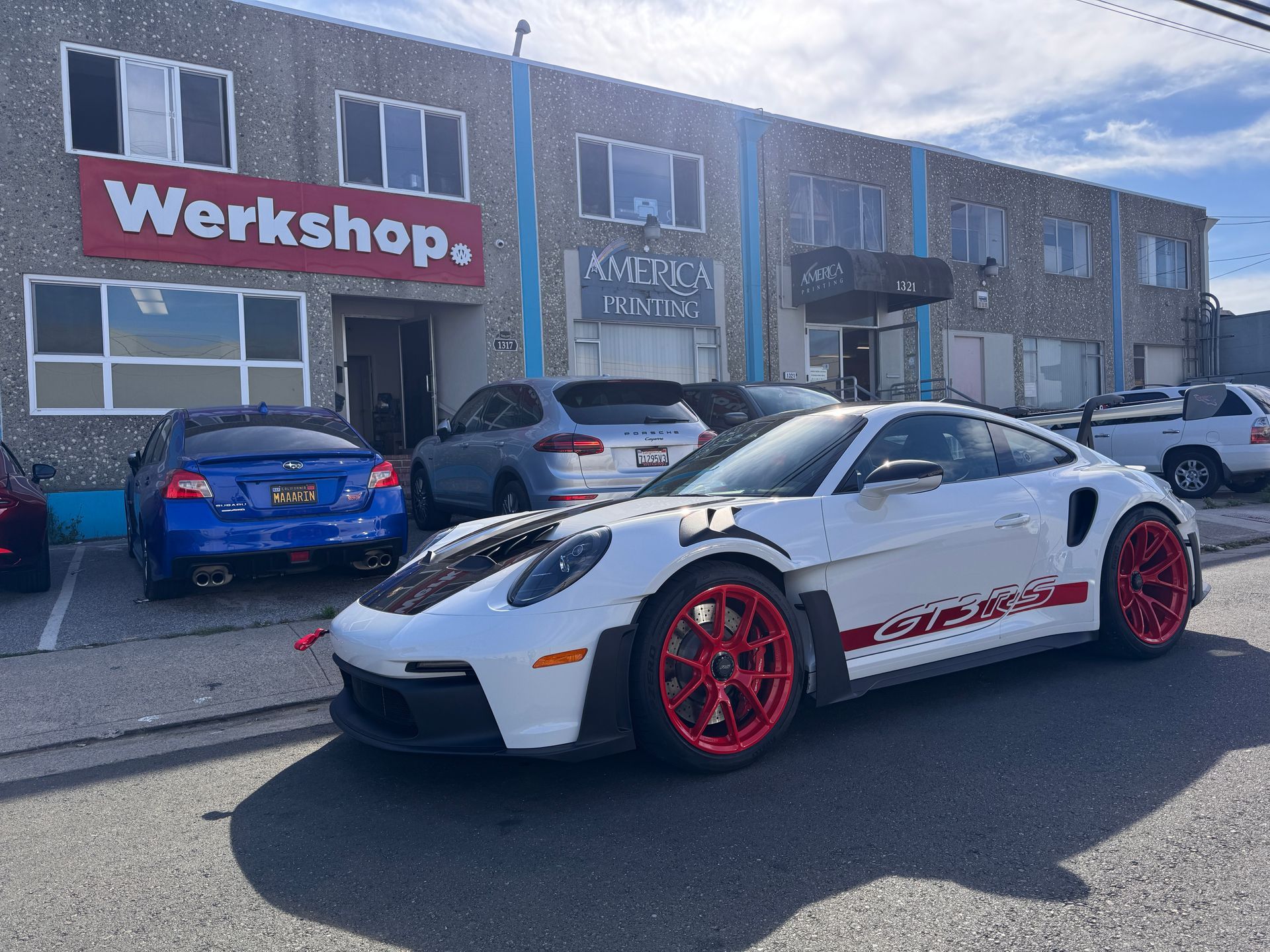 White sports car with red wheels parked outside a workshop storefront.