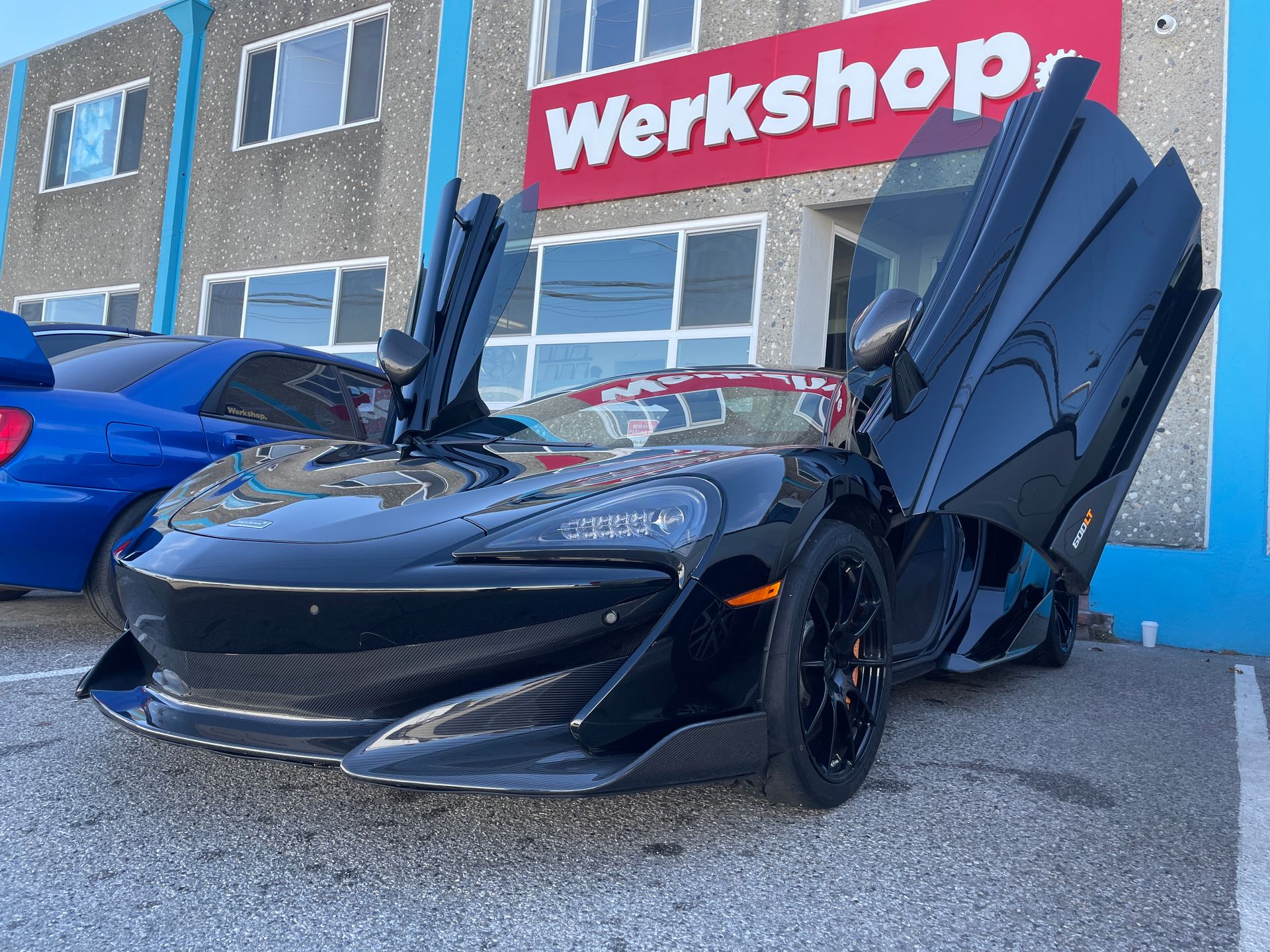 Black sports car with butterfly doors open outside a workshop building