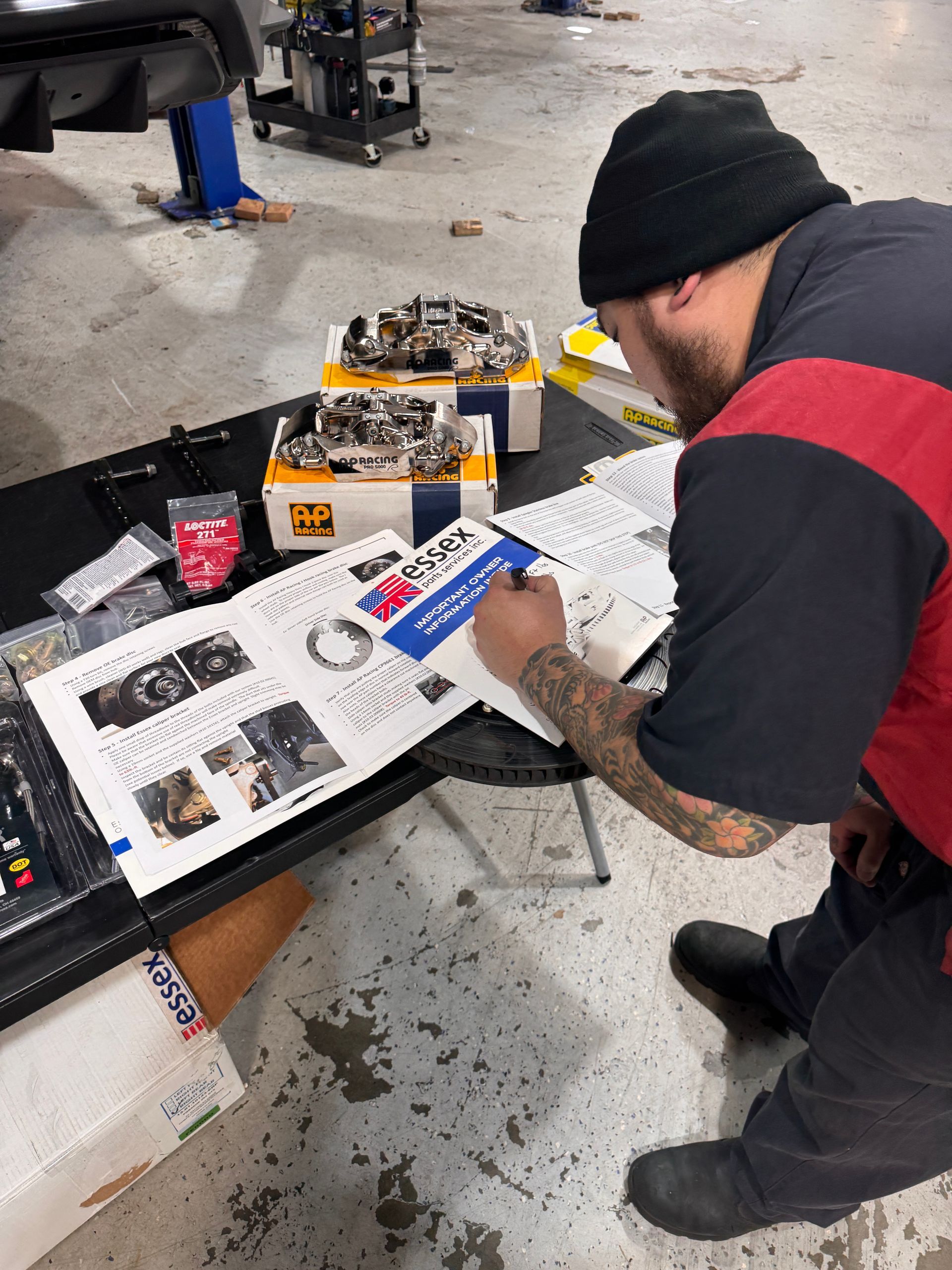 Person leaning over a workbench reviewing papers and parts in a workshop garage