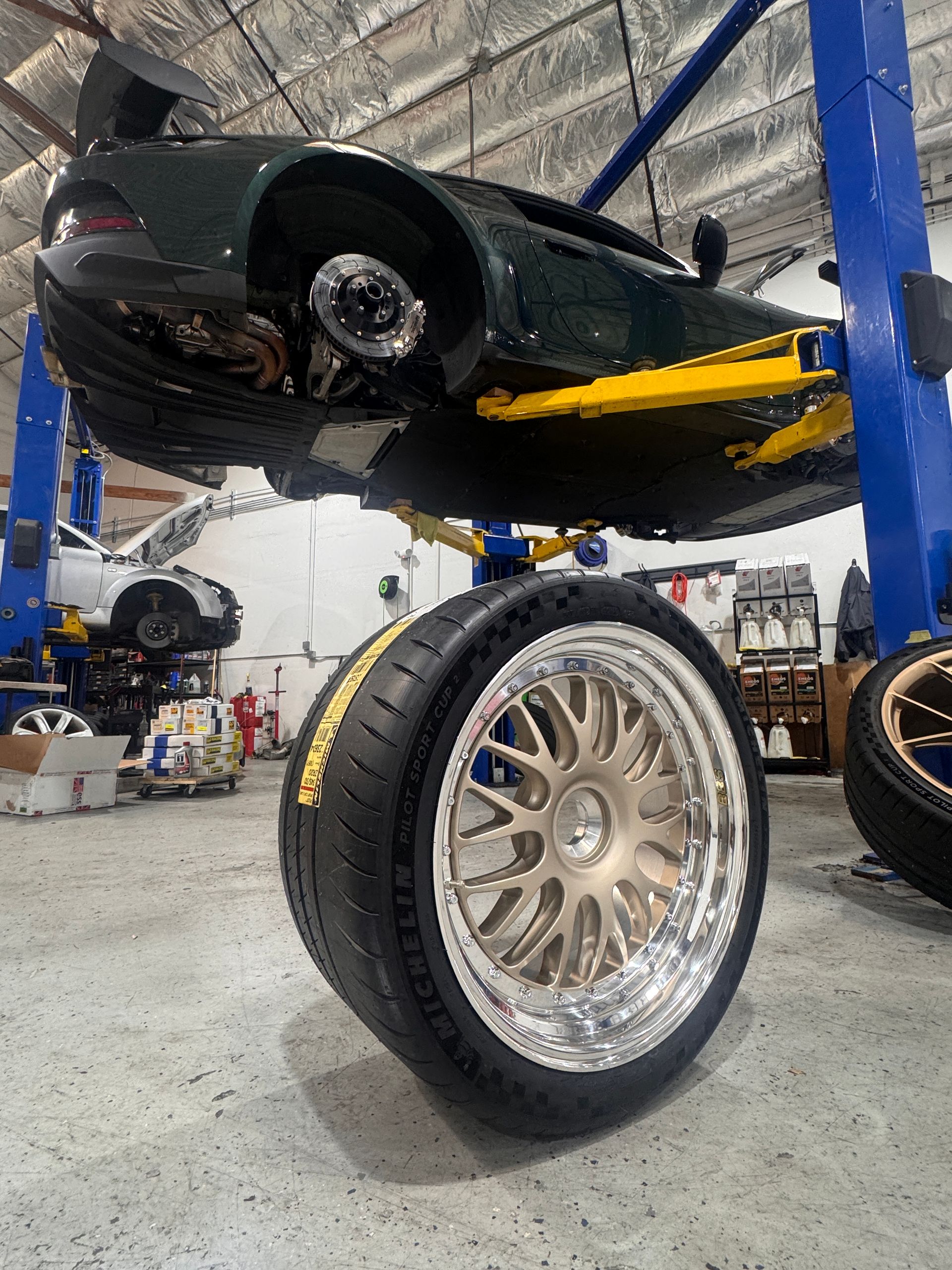 Custom car on a lift in an auto shop, with a large chrome wheel in the foreground
